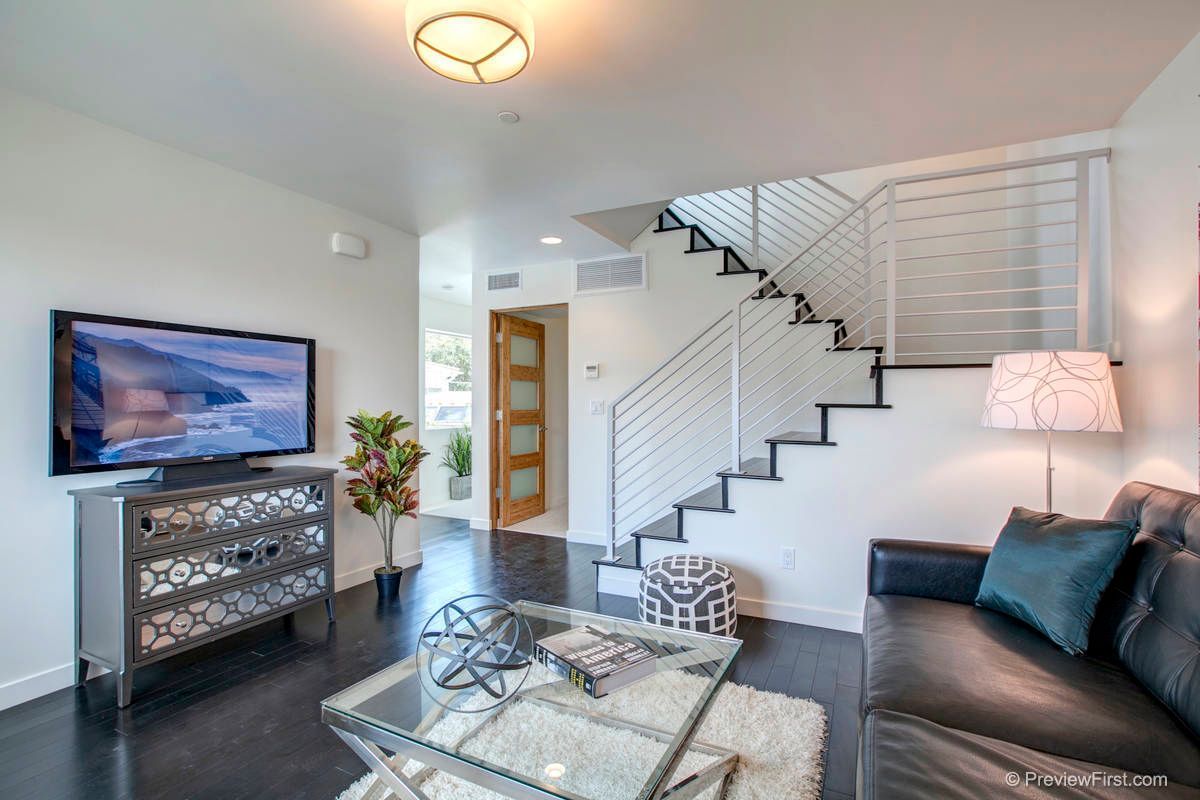 Modern living room with a TV on a decorative cabinet, a glass coffee table, stairs with a metal railing, and a sofa.