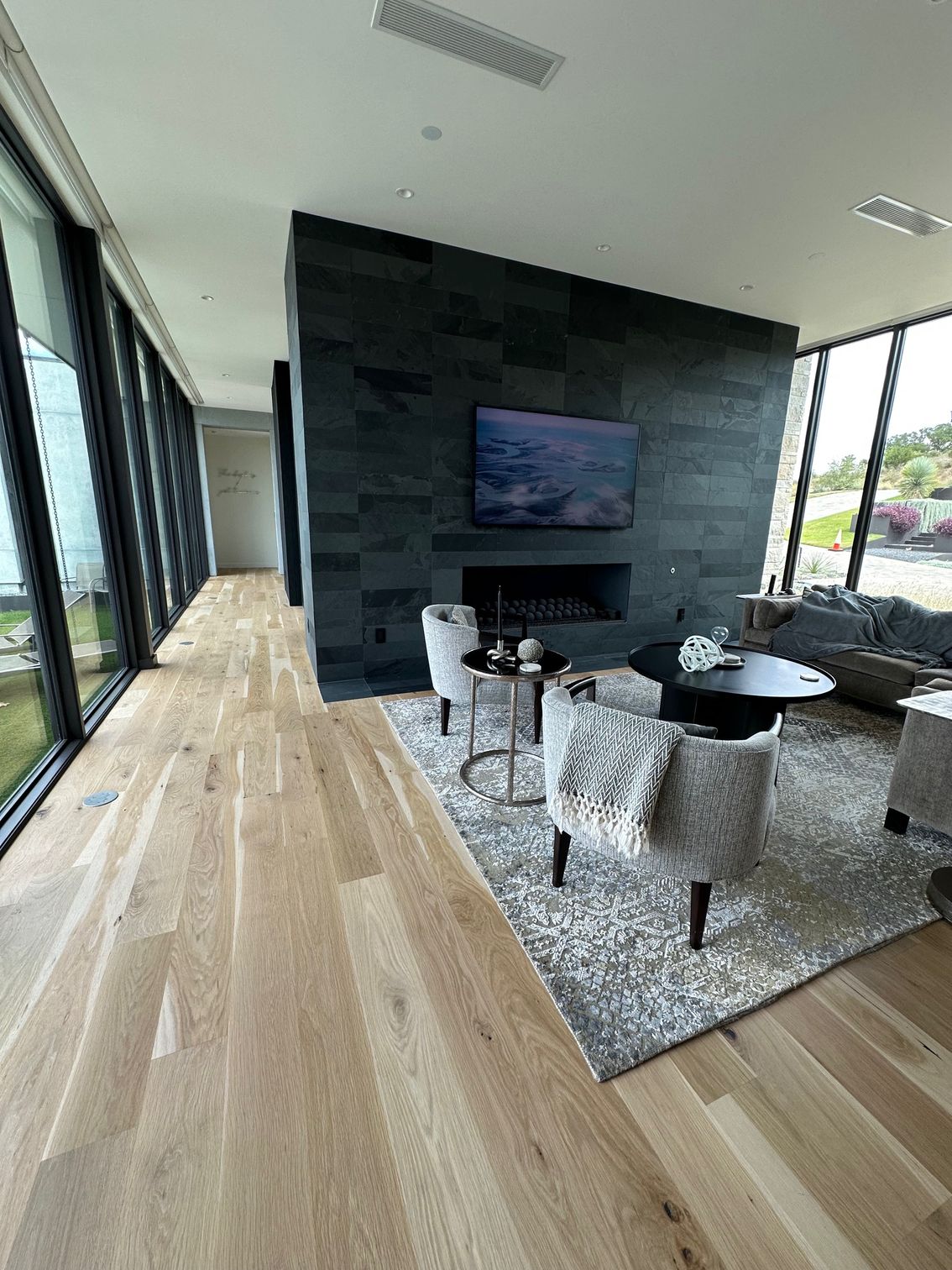 Long hallway with wood floor and large windows overlooking yard and pool. Black wall on the left.