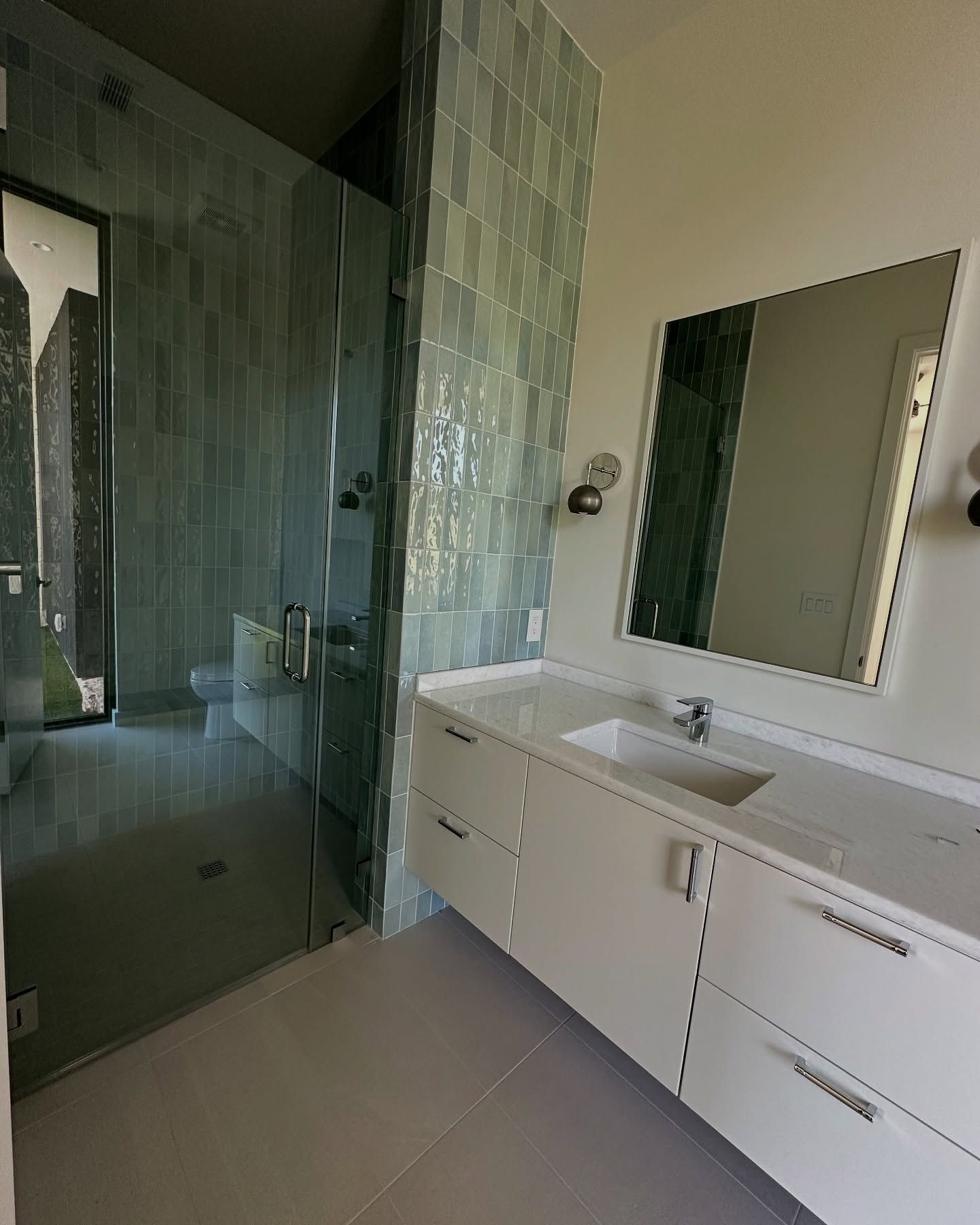 Modern bathroom with glass shower, white vanity, and turquoise tile accents.