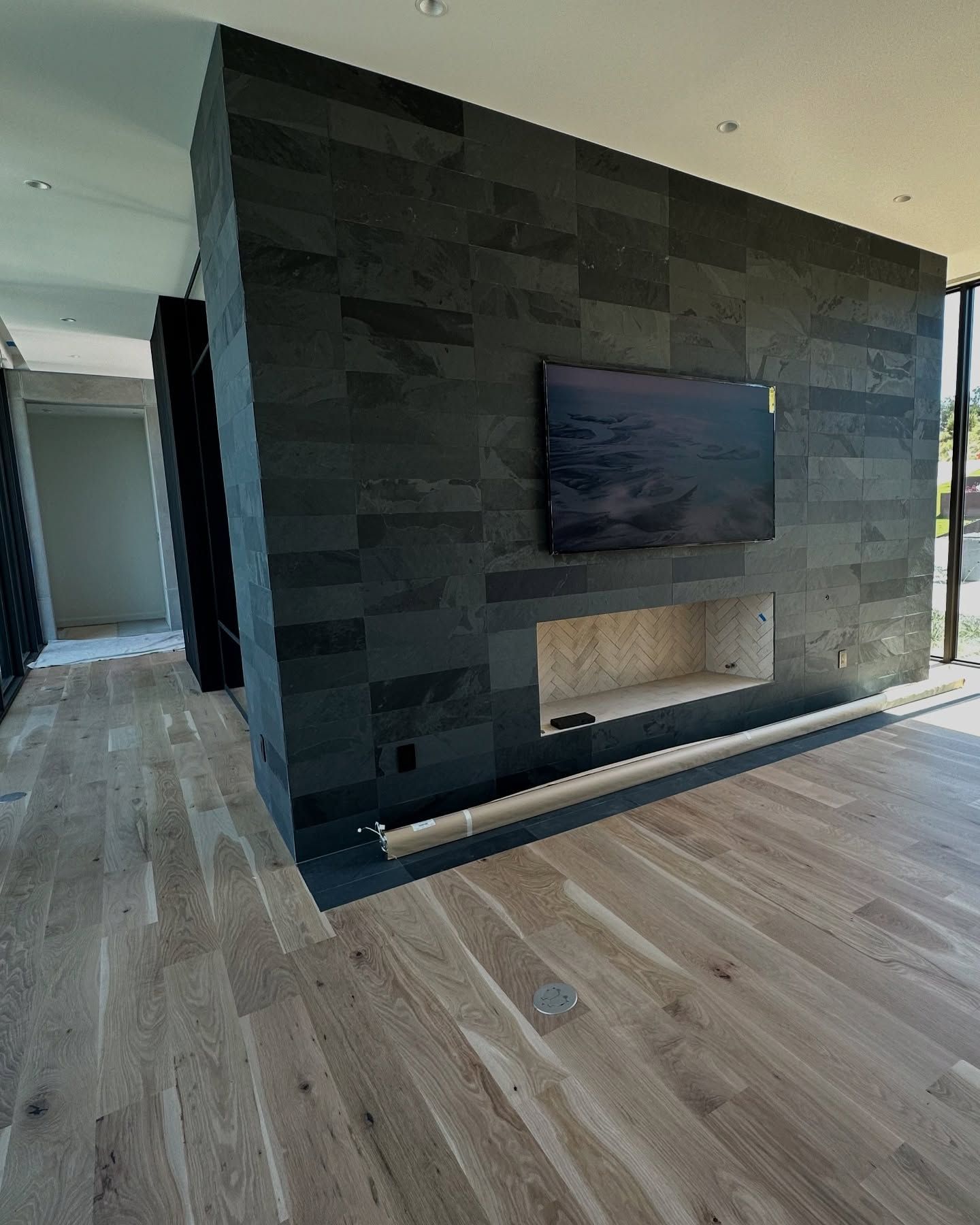 Stone-tiled wall with a fireplace and television. Light wood floor in foreground, open doorway on left.