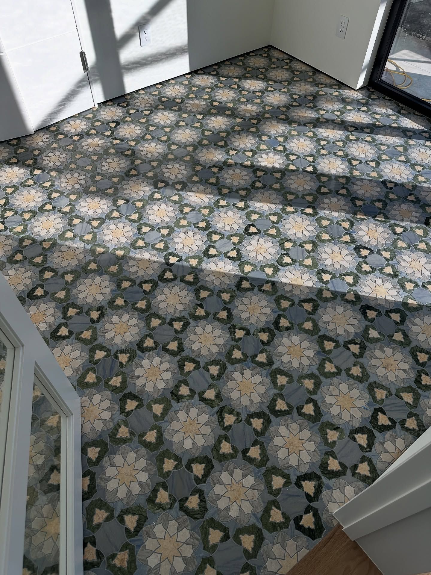 Patterned tile floor in a room, featuring light tan floral designs and dark blue-green geometric shapes.