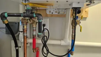 Plumbing pipes and valves mounted on a wall, with a black electrical cable and wooden backing. Plumbing Services in Livonia