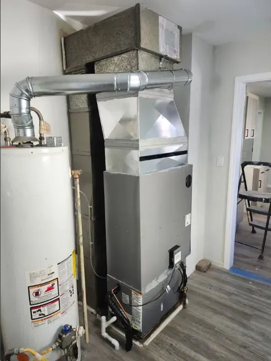 Indoor HVAC furnace and white water heater connected by silver ductwork in a utility room