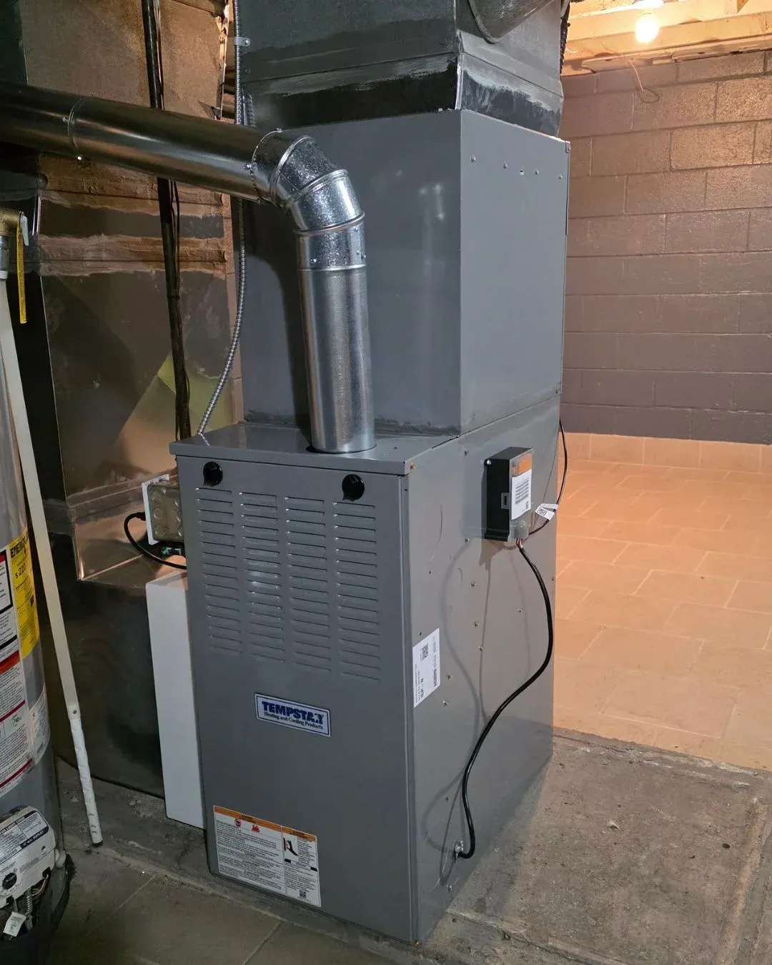 Gray furnace with black ductwork in a basement utility room.