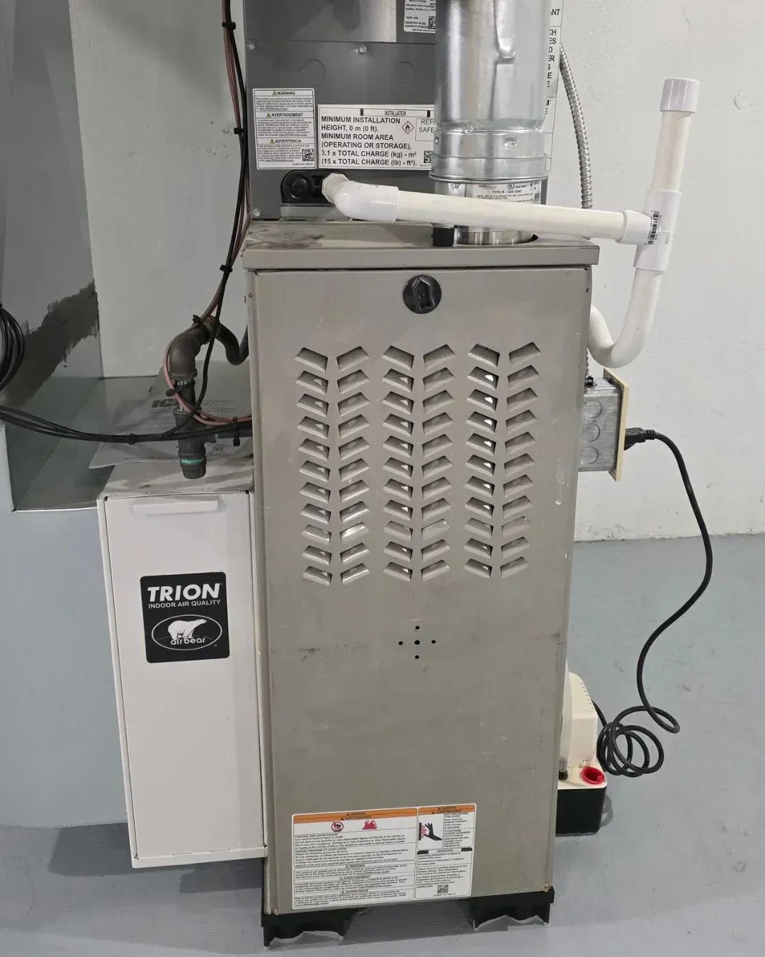 Industrial HVAC furnace with attached ducting and TRION unit in a gray utility room