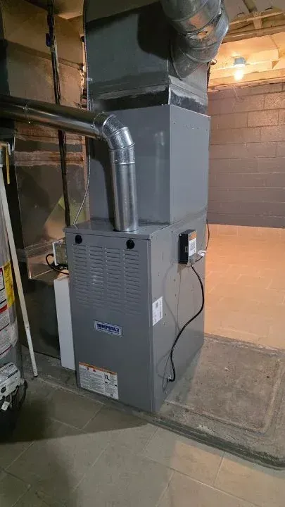 Gray furnace and ductwork in a basement utility room, with a concrete floor and exposed brick walls in Canton, MI.