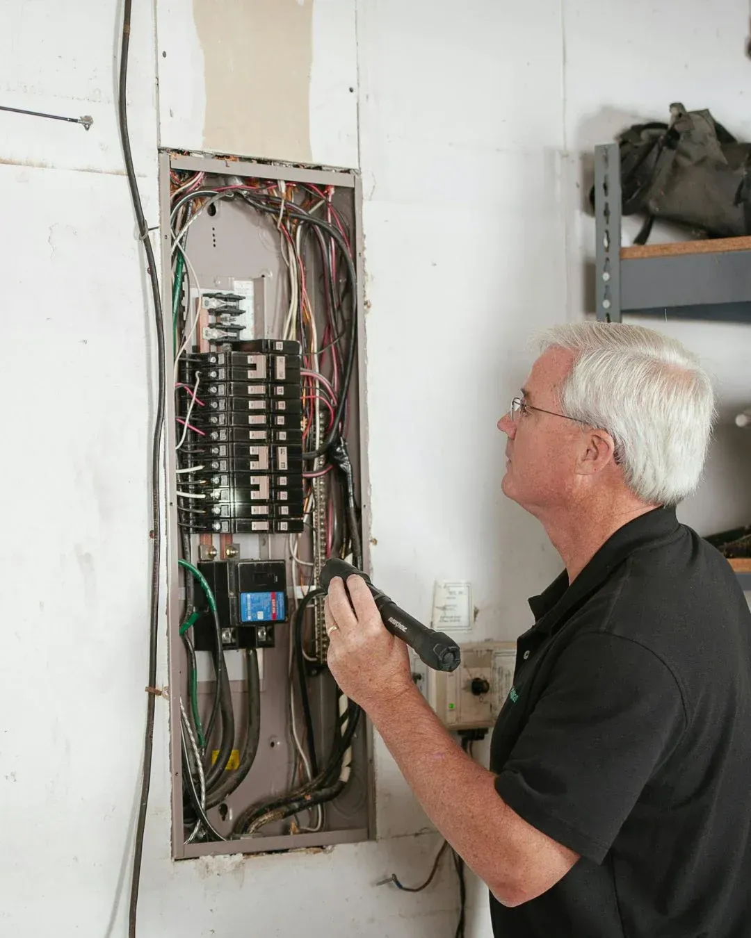 Technician testing an open electrical breaker panel with a meter in a utility room