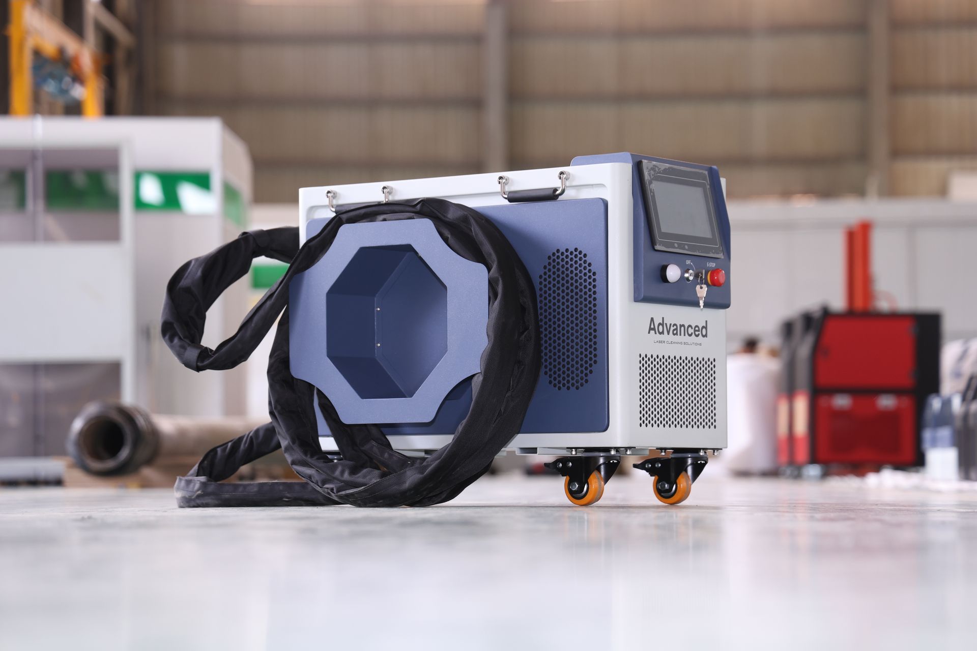 Blue and white industrial laser machine on wheels, with a control panel, hose, and a warehouse background.