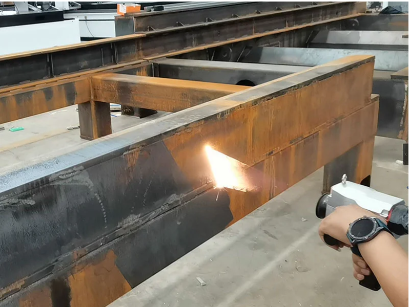 A person using a handheld device to clean rusty steel beams in a workshop. Sparks are visible.