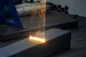 Laser cleaning a metal beam, emitting sparks in a workshop setting.