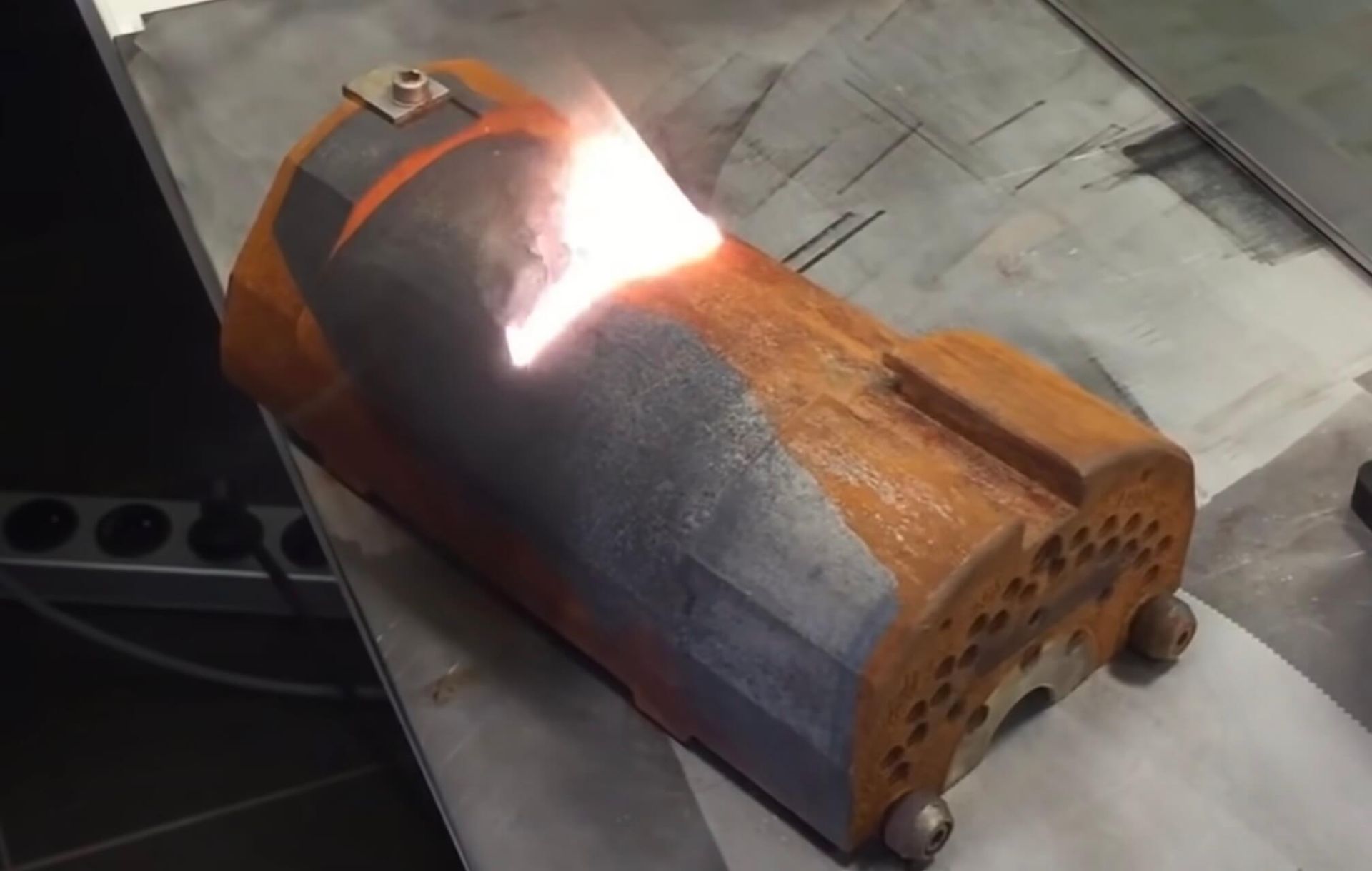 A metal object, likely a furnace, with orange and gray coloring. laser cleaning creating a bright light.