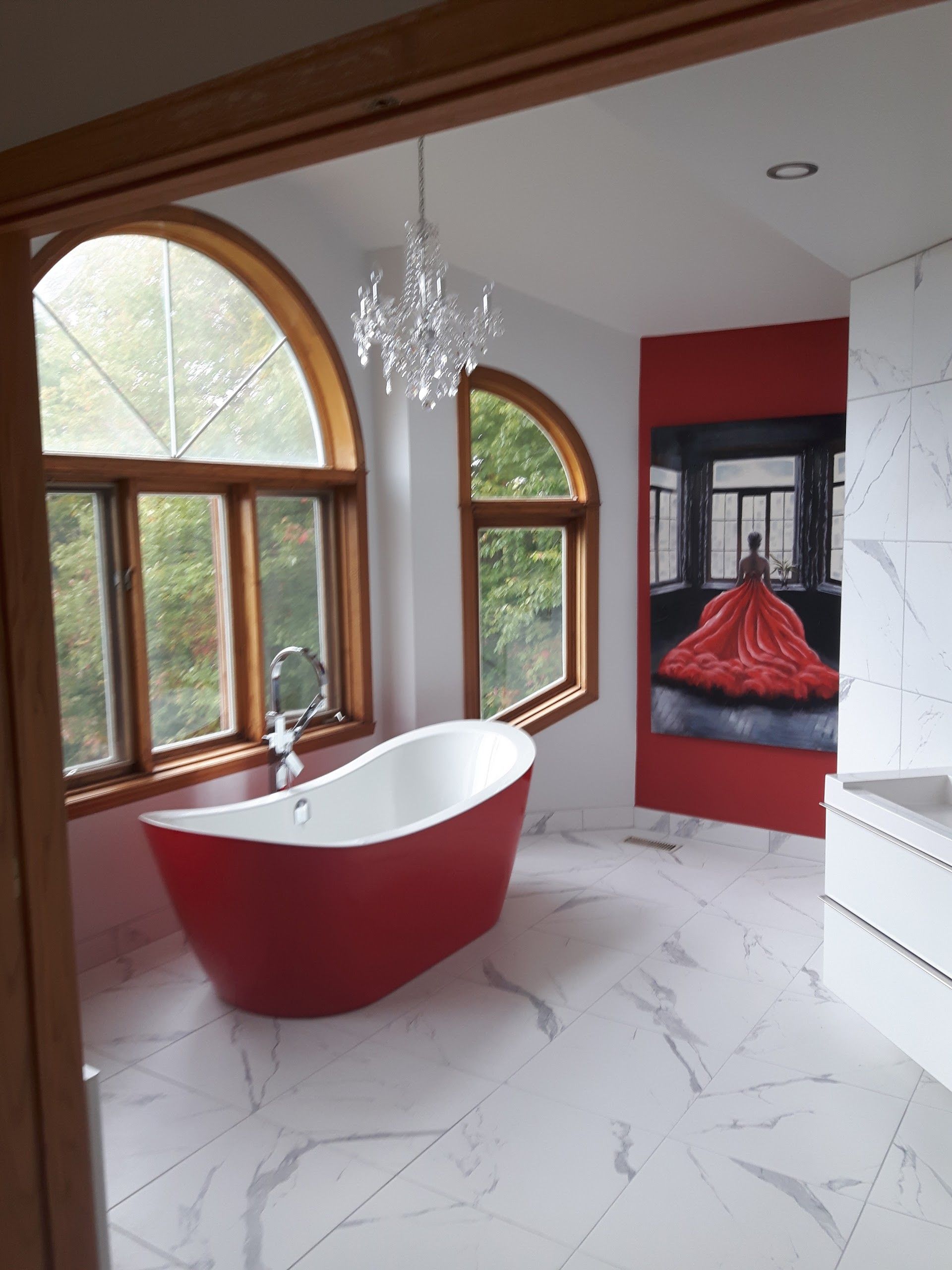 Salle de bains moderne avec baignoire îlot rouge et blanche, fenêtres cintrées et sol en marbre