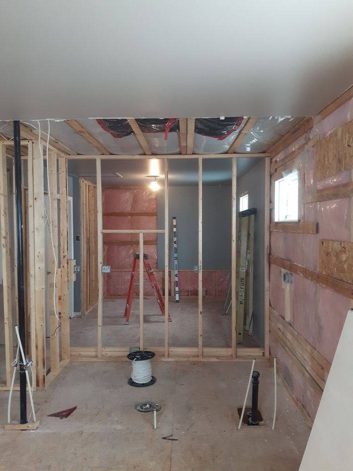 Pièce partiellement ossature bois en cours de rénovation, avec montants apparents, isolation et une échelle au fond.