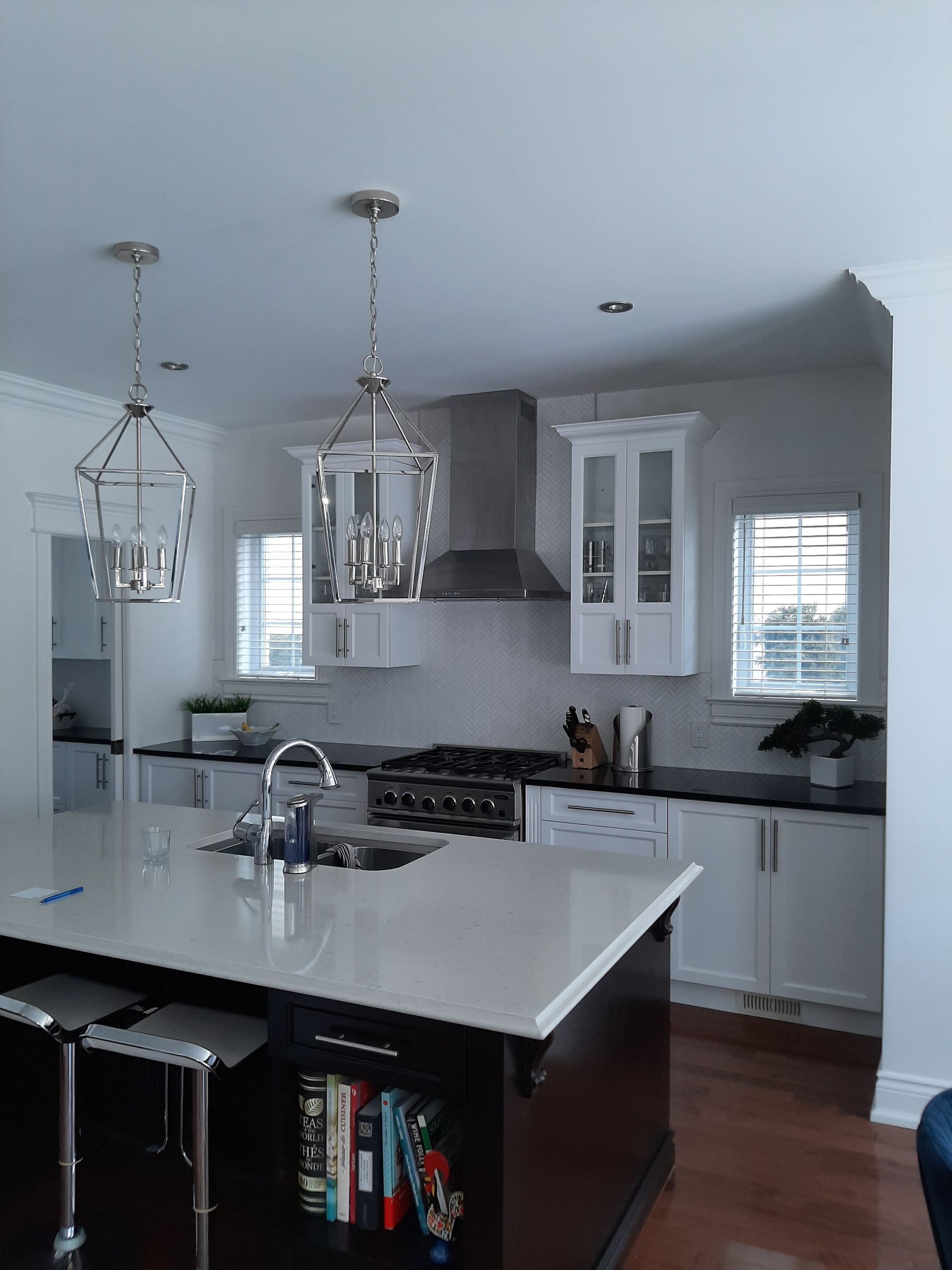 Cuisine moderne avec armoires blanches, îlot noir, hotte en inox et luminaires suspendus