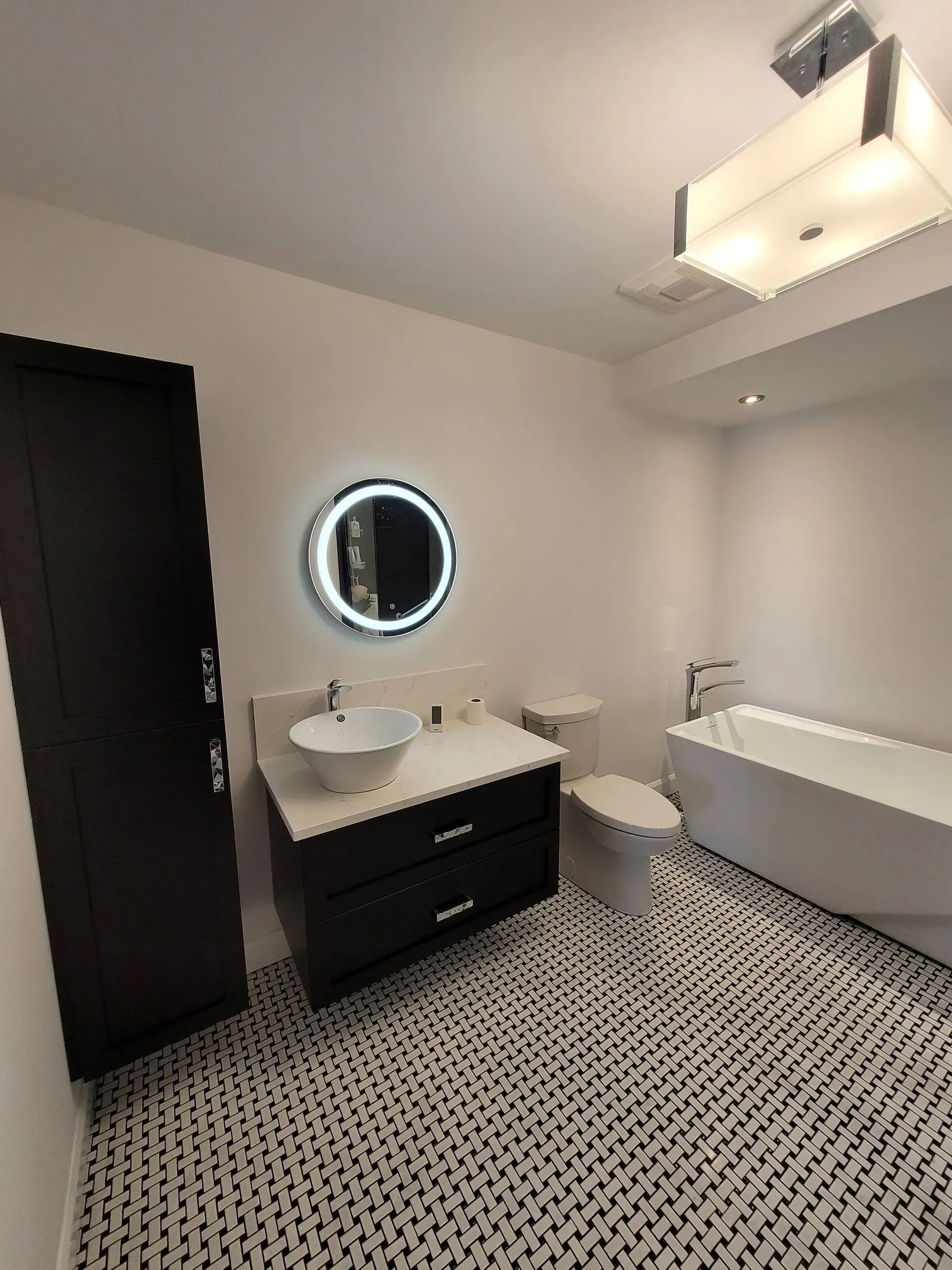 Salle de bains moderne avec meuble-lavabo noir, miroir rond, toilettes et carrelage à motifs au sol