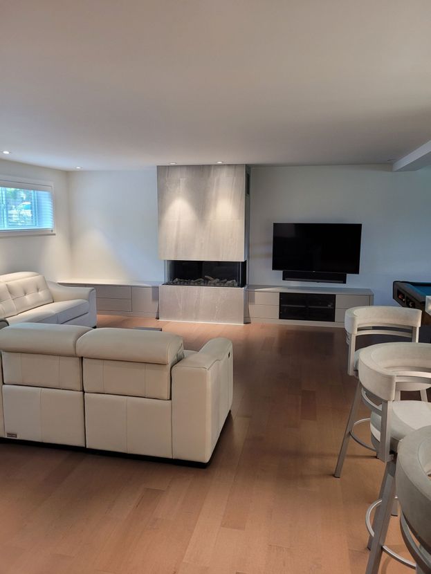 Salon moderne avec canapés blancs, parquet, télévision murale et grande fenêtre.