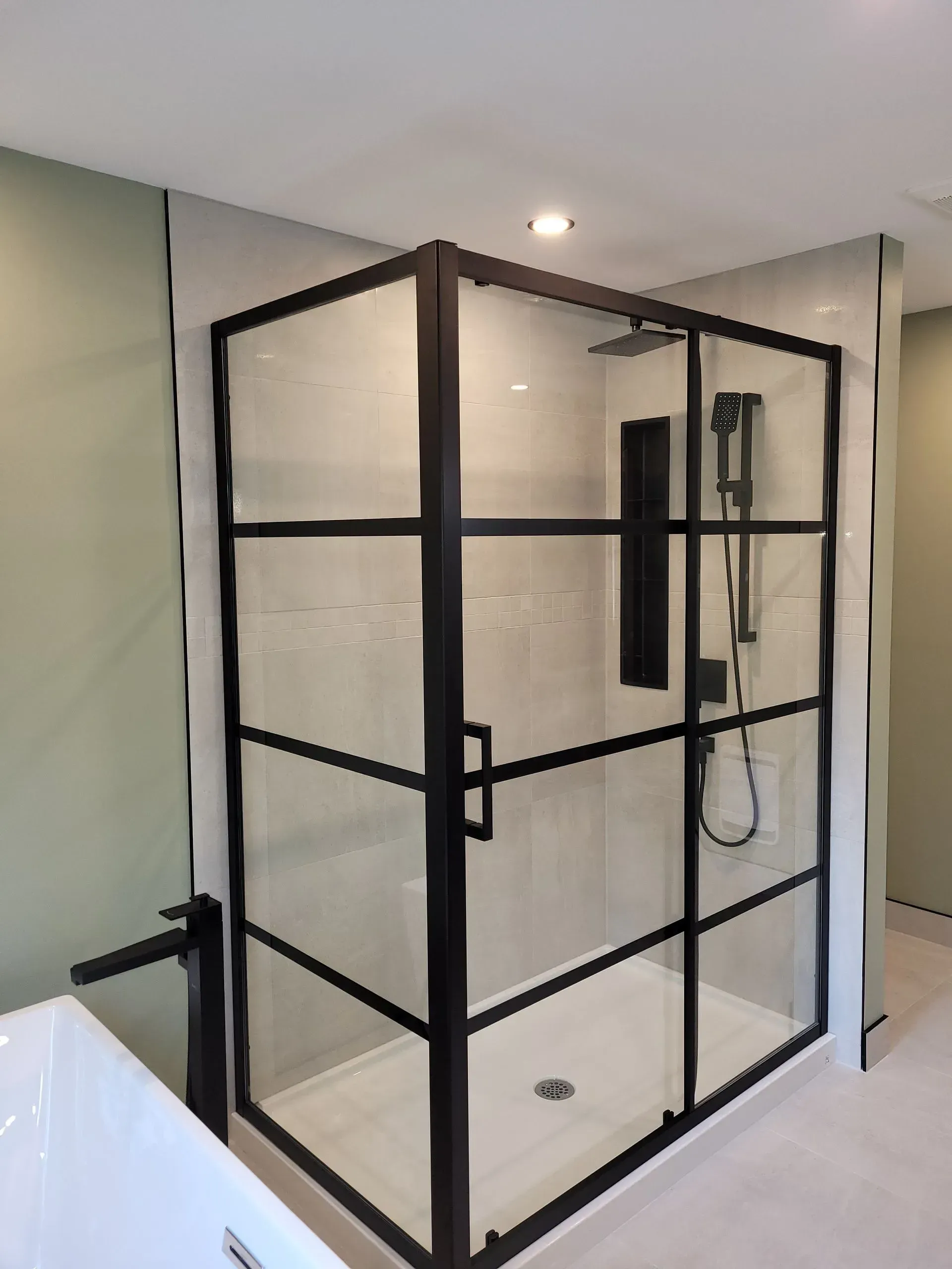 Cabine de douche en verre à cadre noir dans une salle de bain moderne carrelée de blanc avec douchette.
