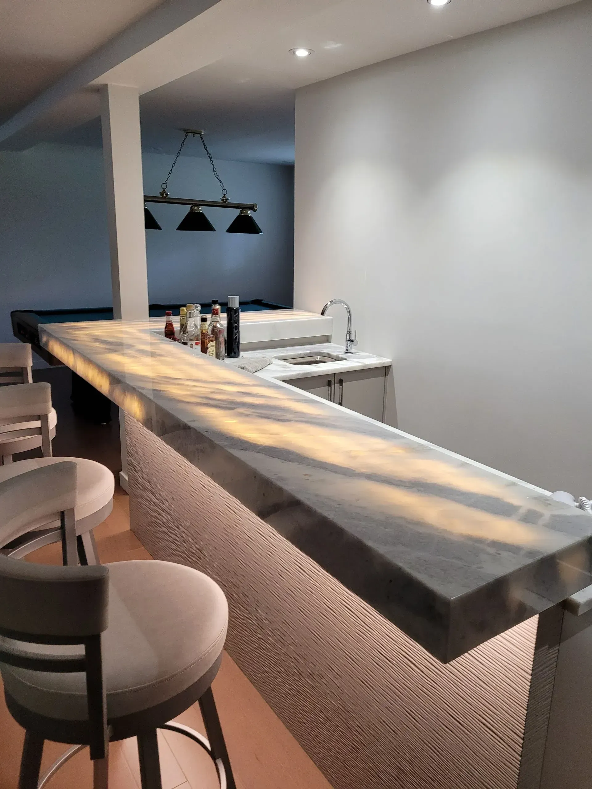 Intérieur de bar moderne avec un long comptoir en pierre, des suspensions lumineuses et des tabourets blancs.