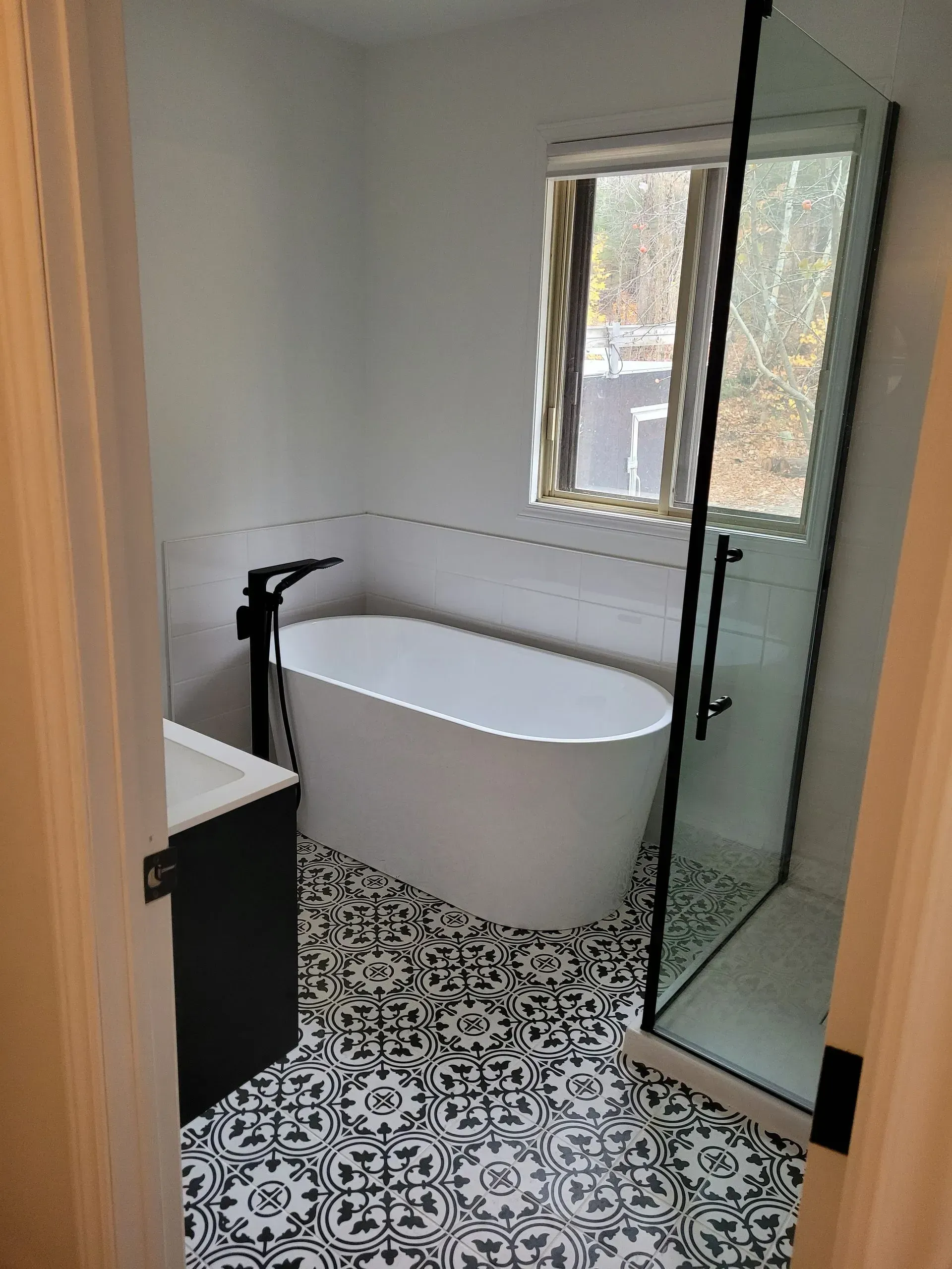 Salle de bains moderne avec baignoire îlot, douche en verre et sol carrelé à motifs noirs et blancs