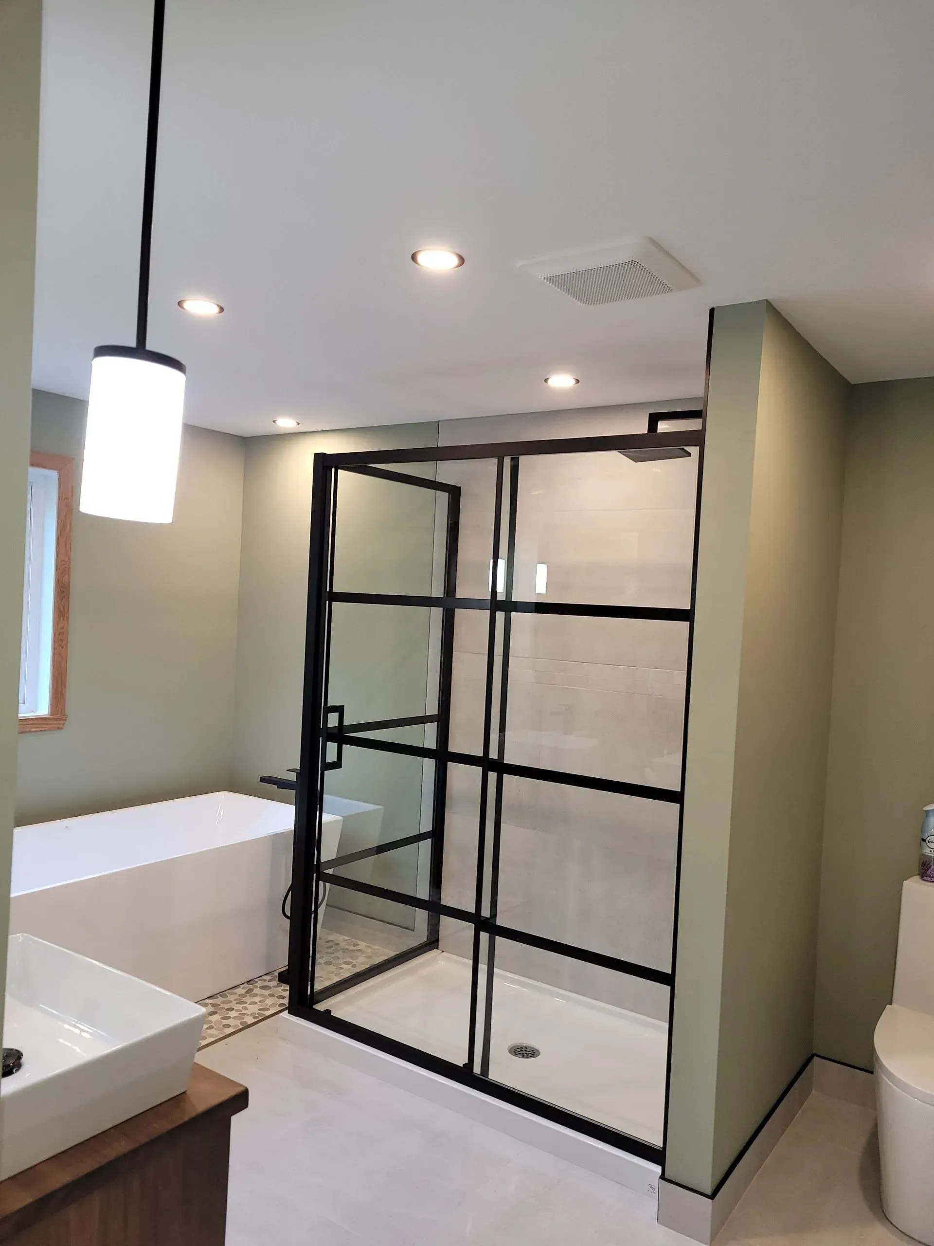 Salle de bains moderne avec une cabine de douche en verre à cadre noir, une baignoire blanche et des spots encastrés au plafond.