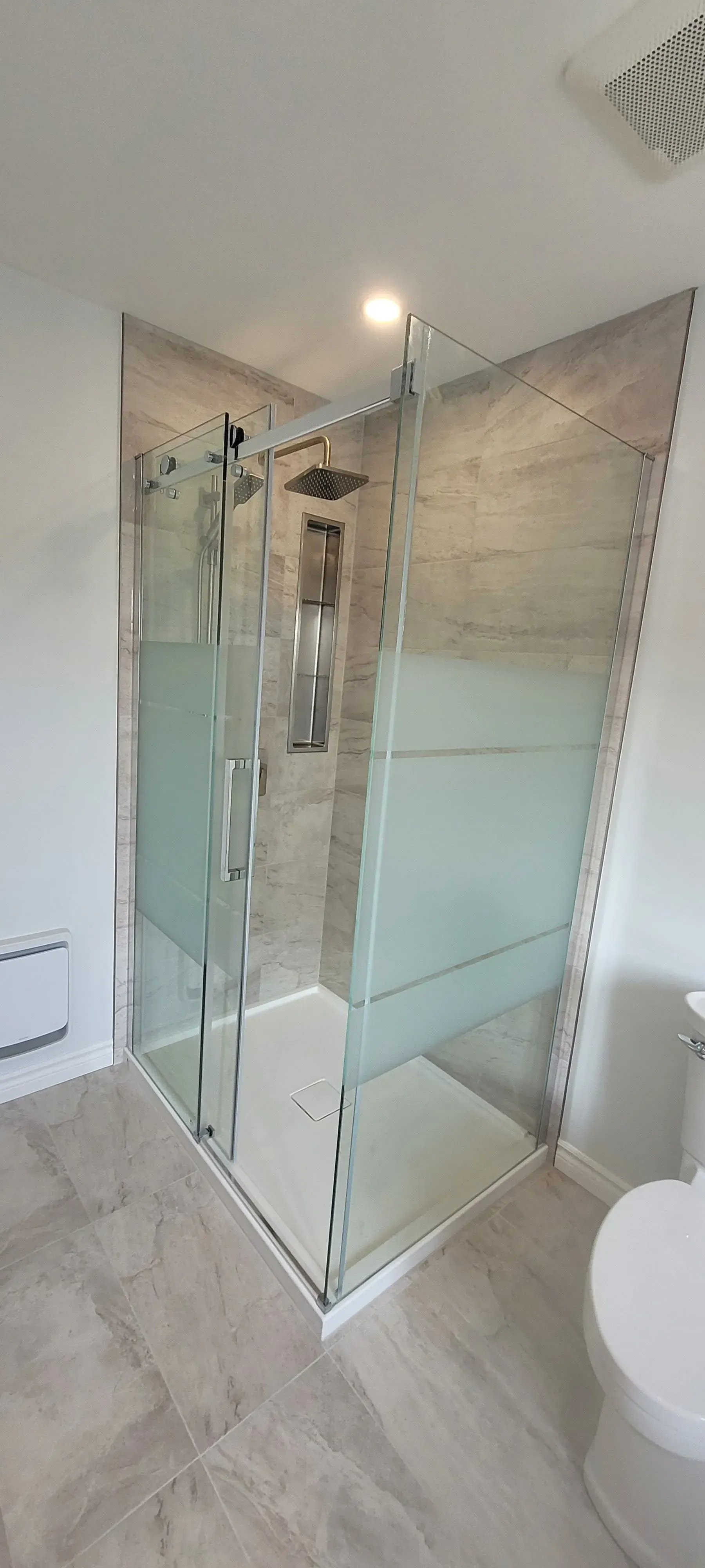 Cabine de douche en verre dans une salle de bains carrelée de blanc, avec panneaux inférieurs dépolis et robinetterie chromée.