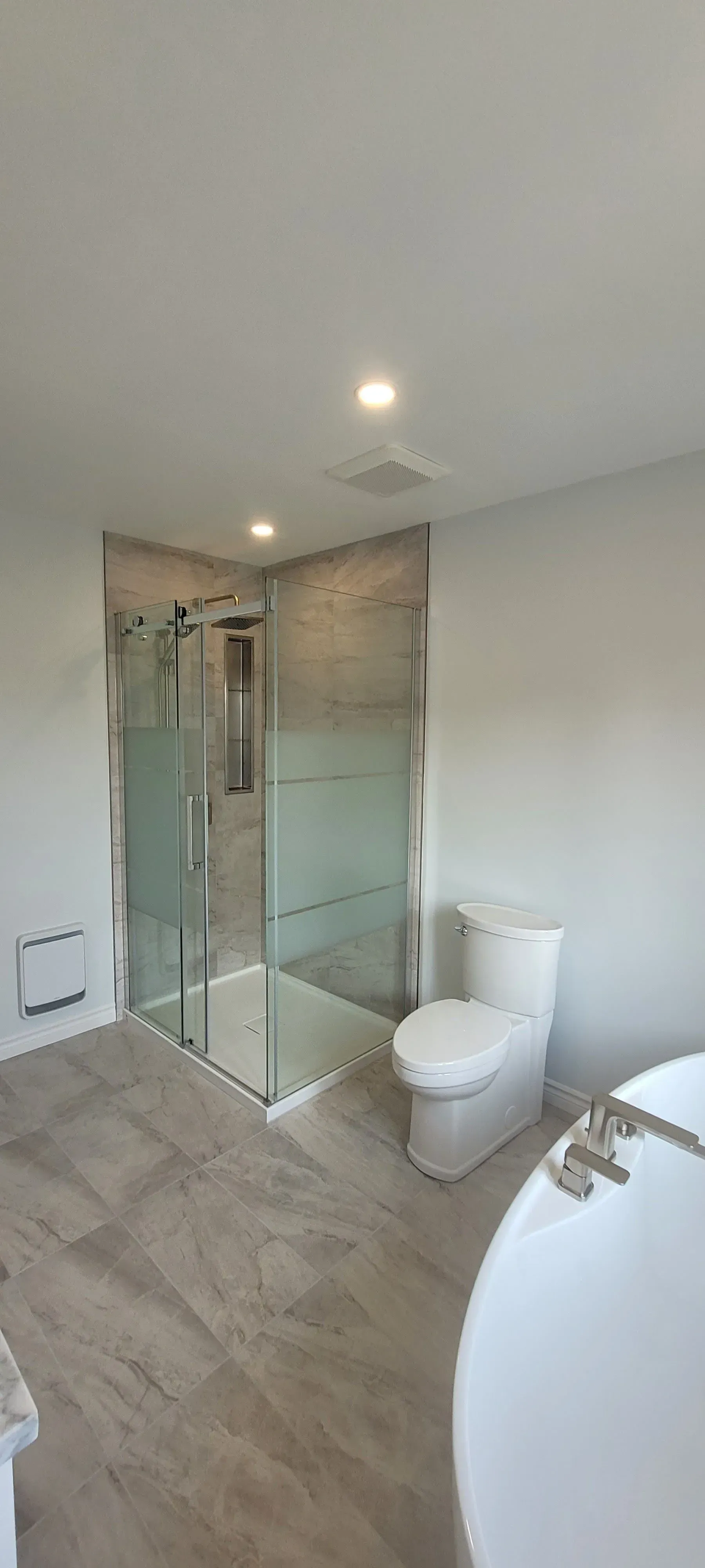 Salle de bains moderne avec douche en verre, toilettes blanches et baignoire îlot sur sol carrelé imitation bois