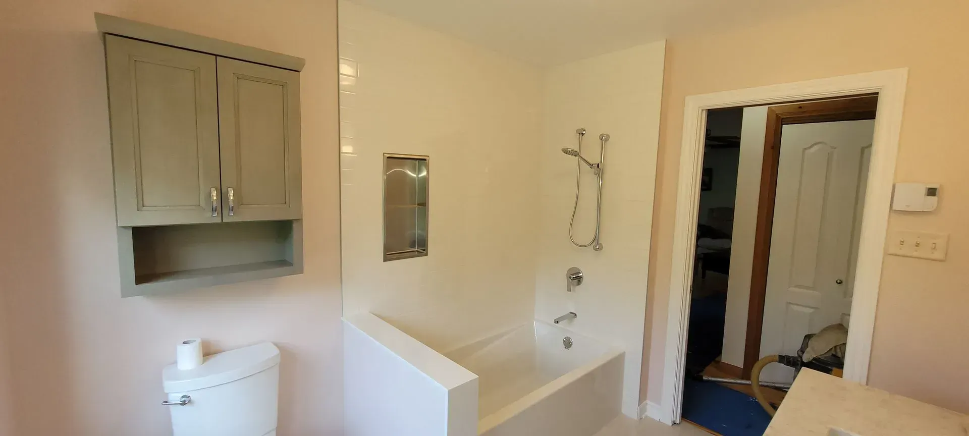 Petite salle de bains avec toilettes, baignoire, armoire de toilette, porte-serviettes et porte ouverte sur un couloir.