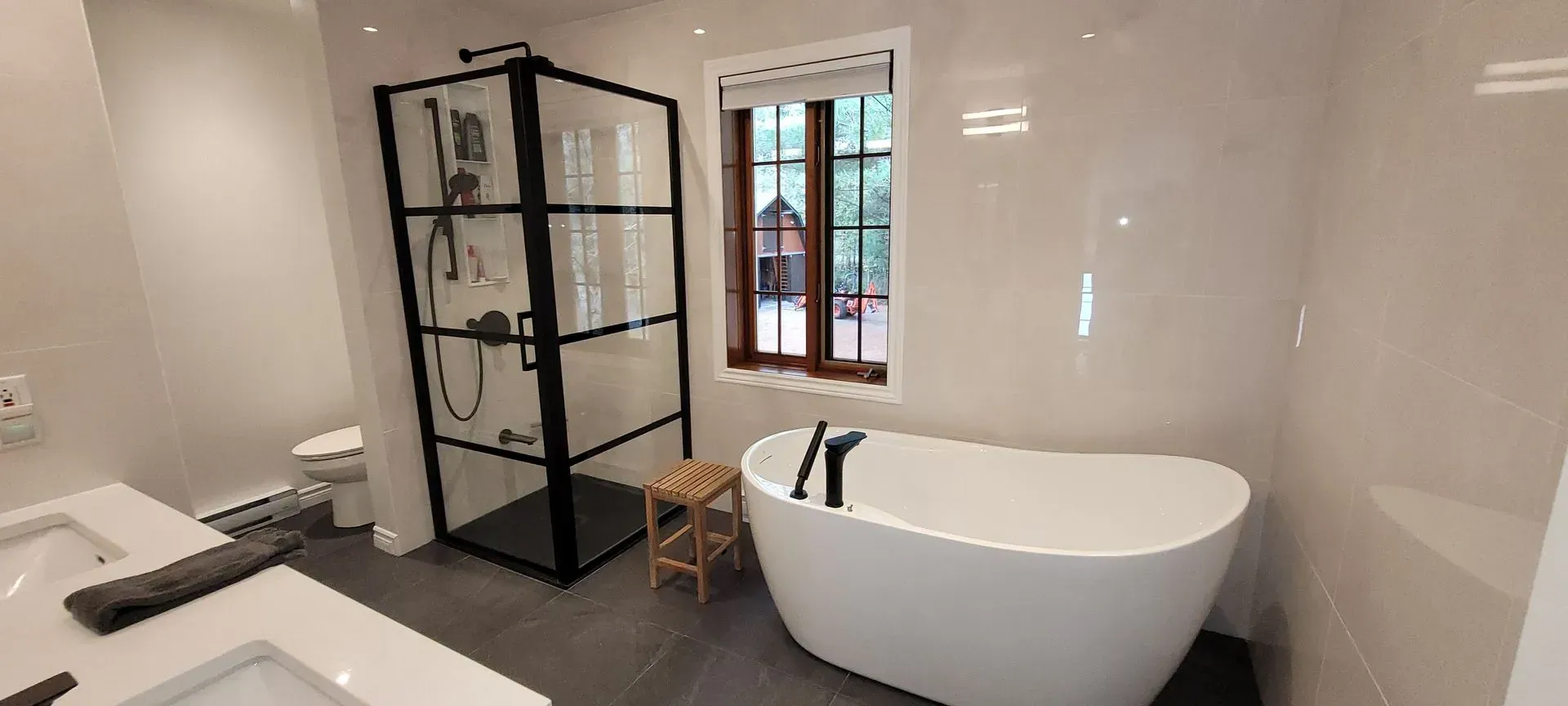 Salle de bains moderne avec baignoire îlot, douche vitrée et meuble-lavabo foncé sur sol carrelé gris