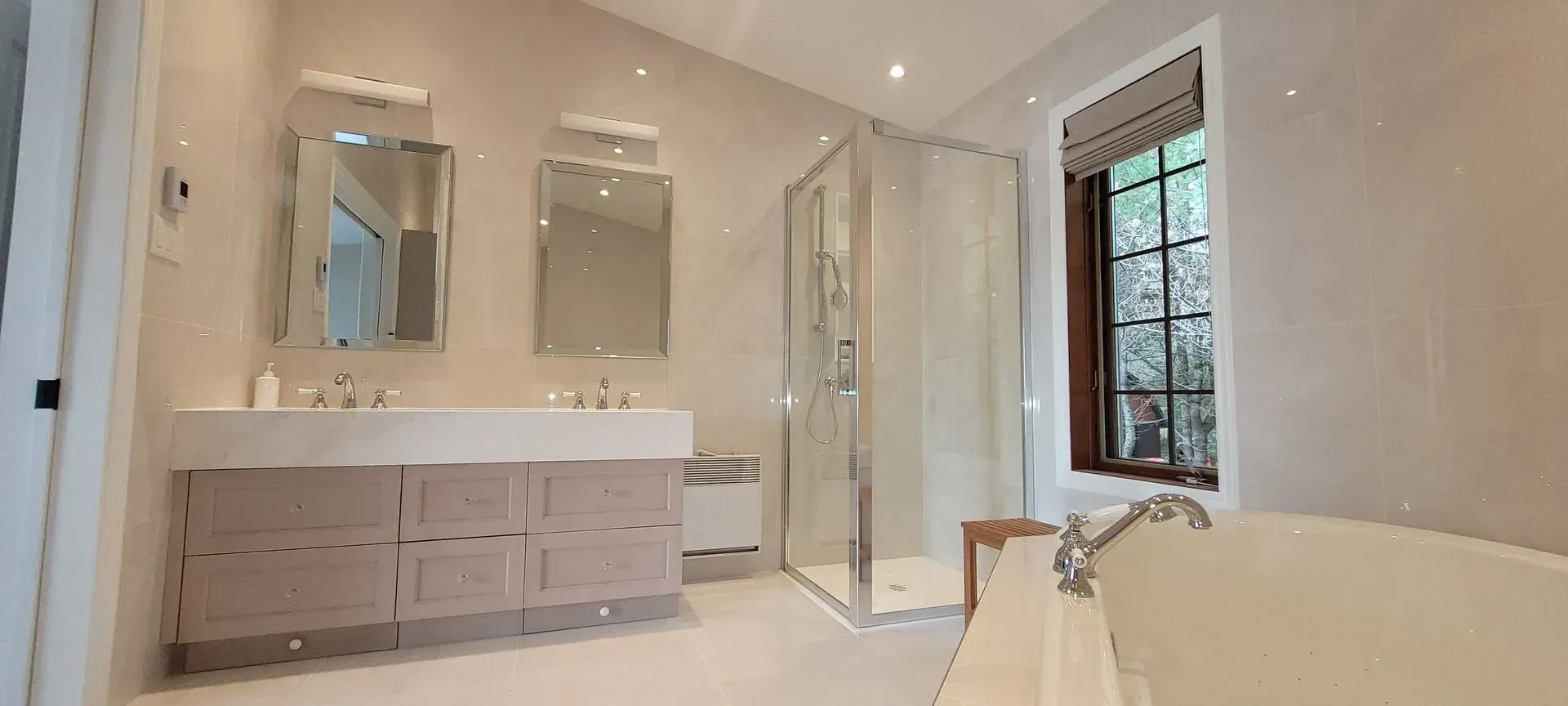 Salle de bains luxueuse et lumineuse avec double vasque, miroirs, douche à l'italienne et baignoire îlot près d'une fenêtre