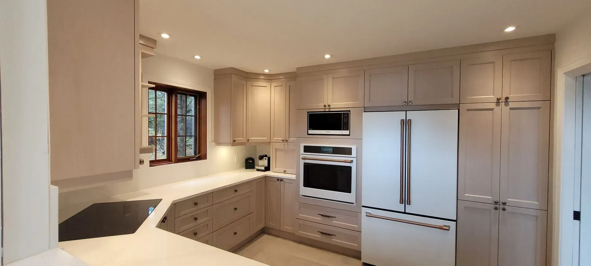 Cuisine moderne et lumineuse avec armoires en bois clair, électroménagers blancs et éclairage encastré