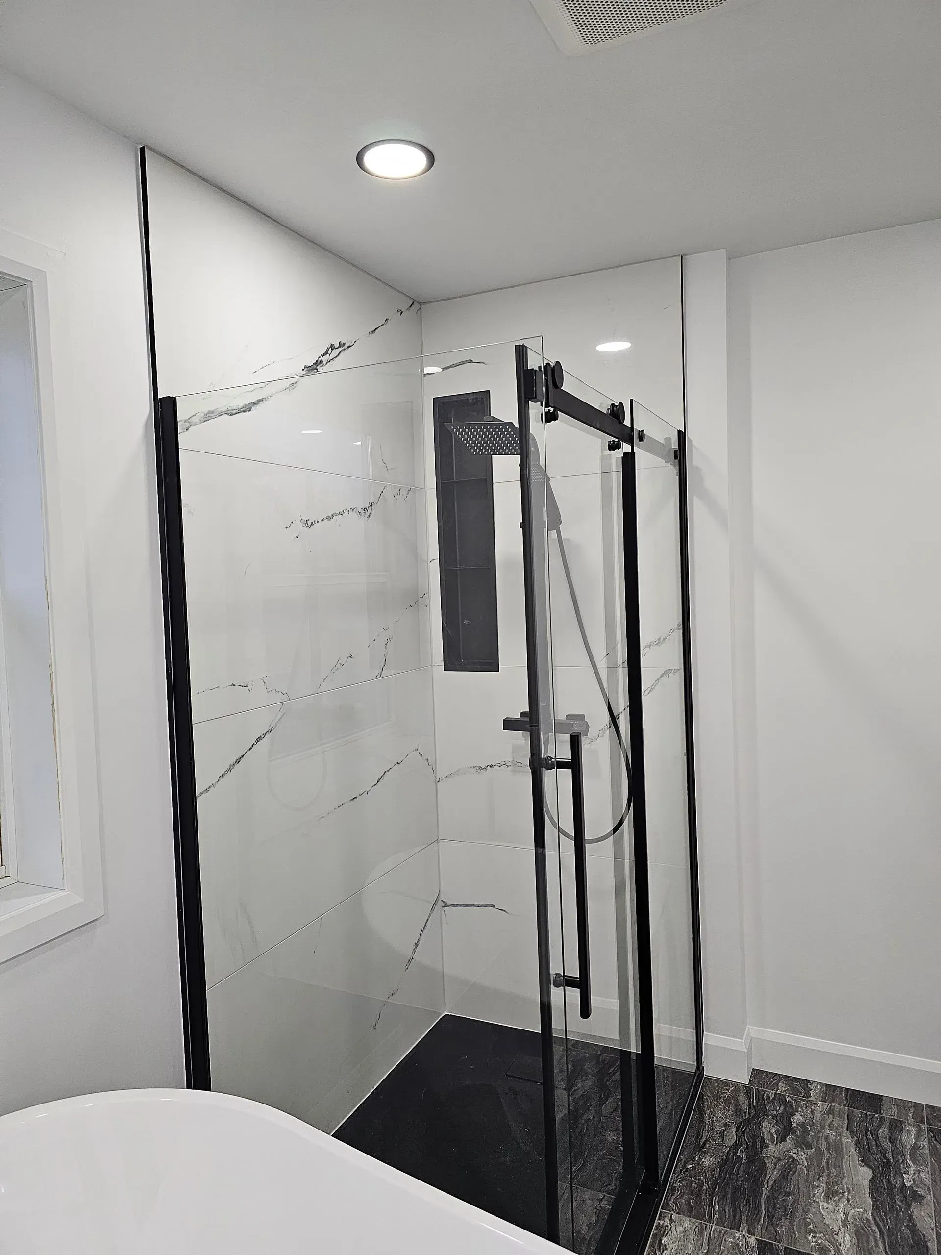 Salle de bains moderne avec cabine de douche en verre, robinetterie noire et murs carrelés blancs