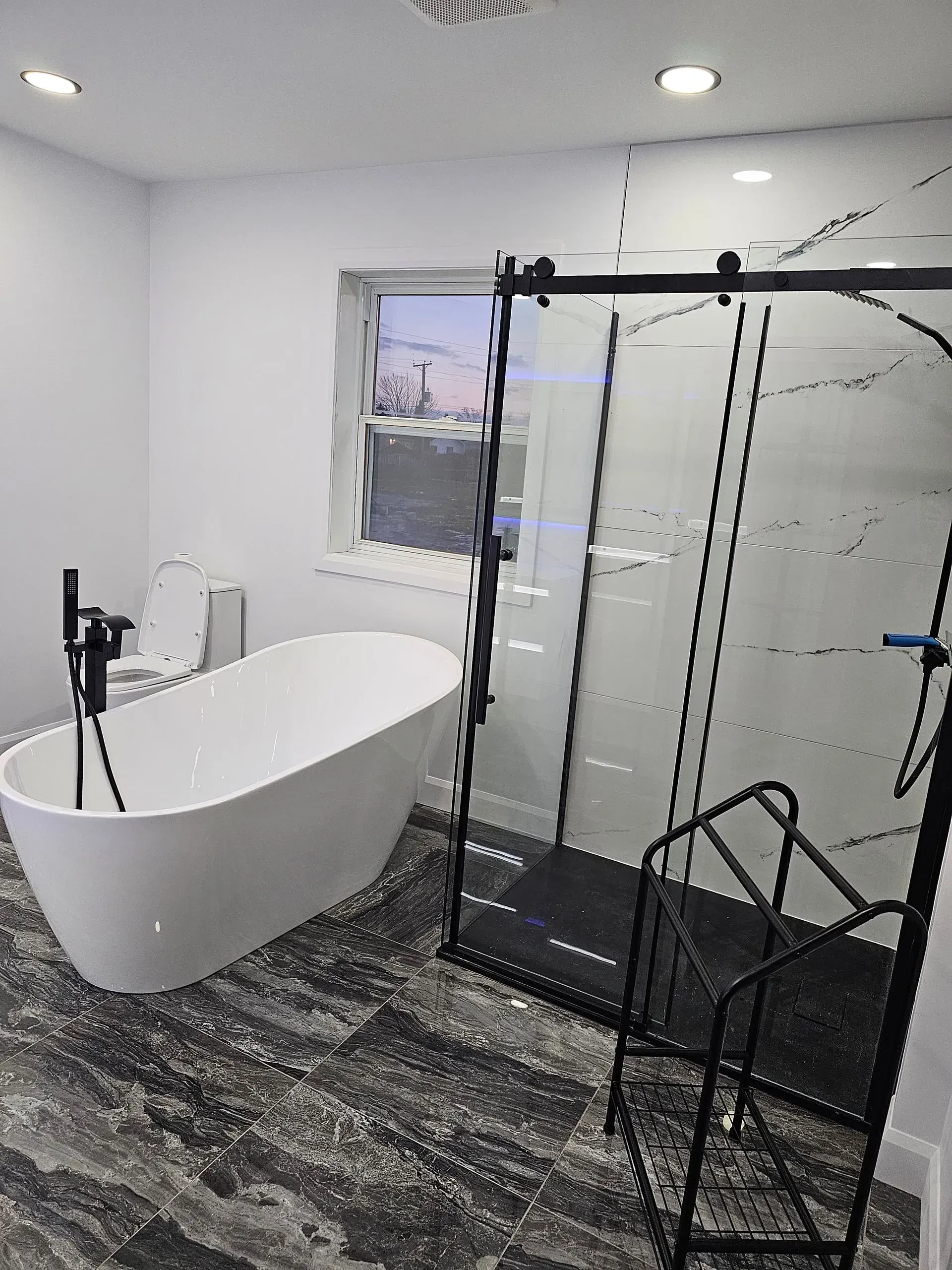 Salle de bains moderne avec baignoire îlot, douche à l'italienne et sol carrelé noir ; trépied visible au premier plan
