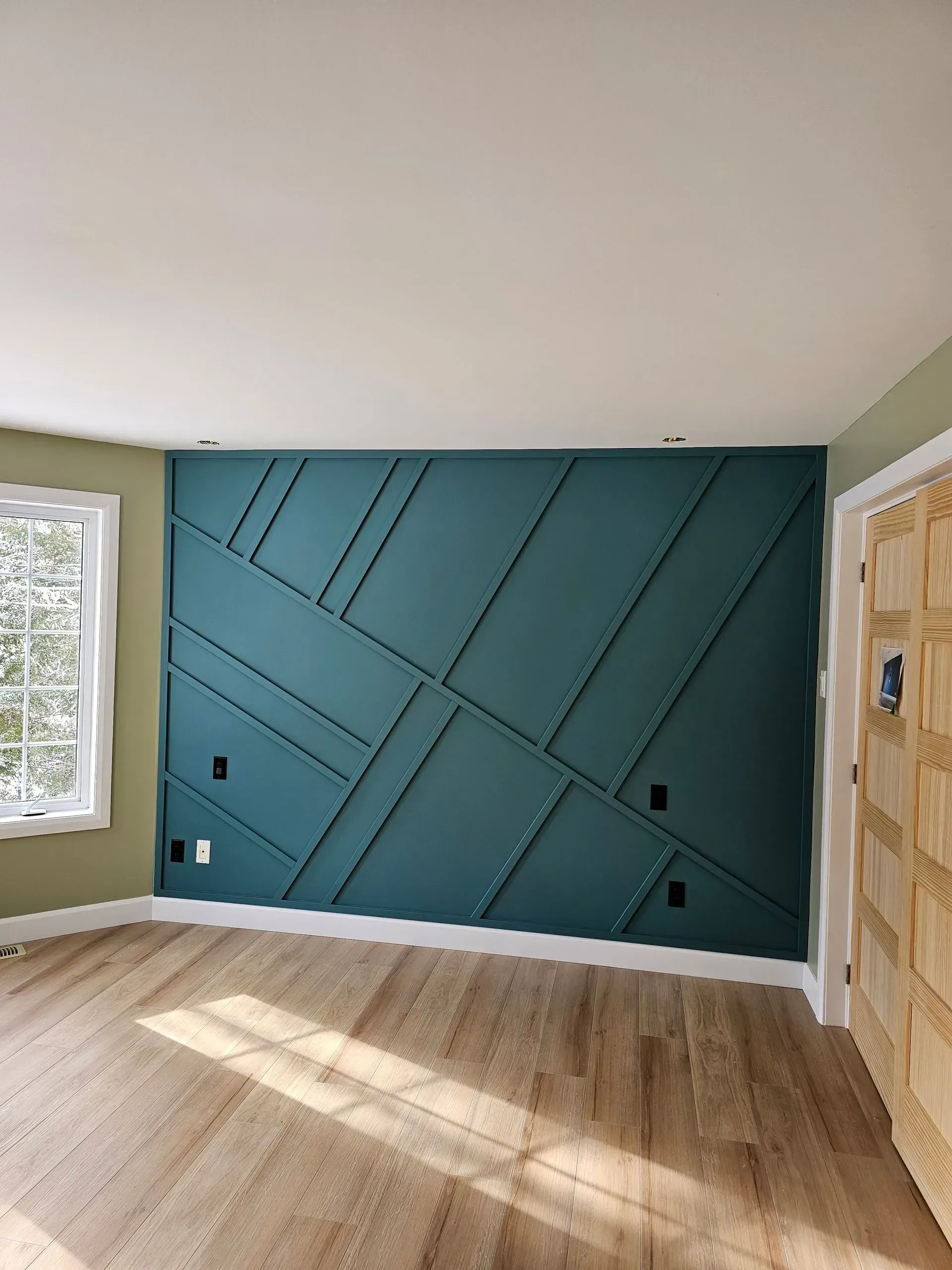 Pièce vide avec un mur d'accent géométrique turquoise, un parquet clair et la lumière du soleil entrant par les fenêtres.