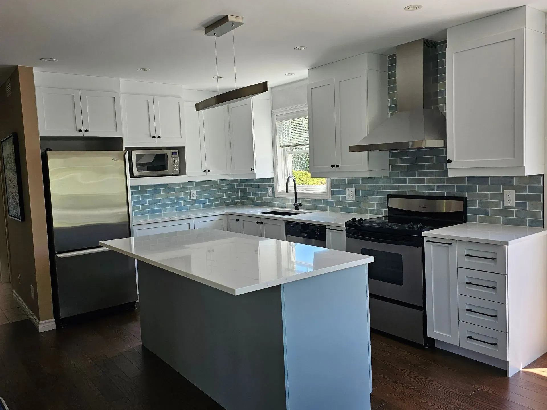 Cuisine moderne blanche avec électroménagers en acier inoxydable, crédence en carrelage bleu et parquet foncé