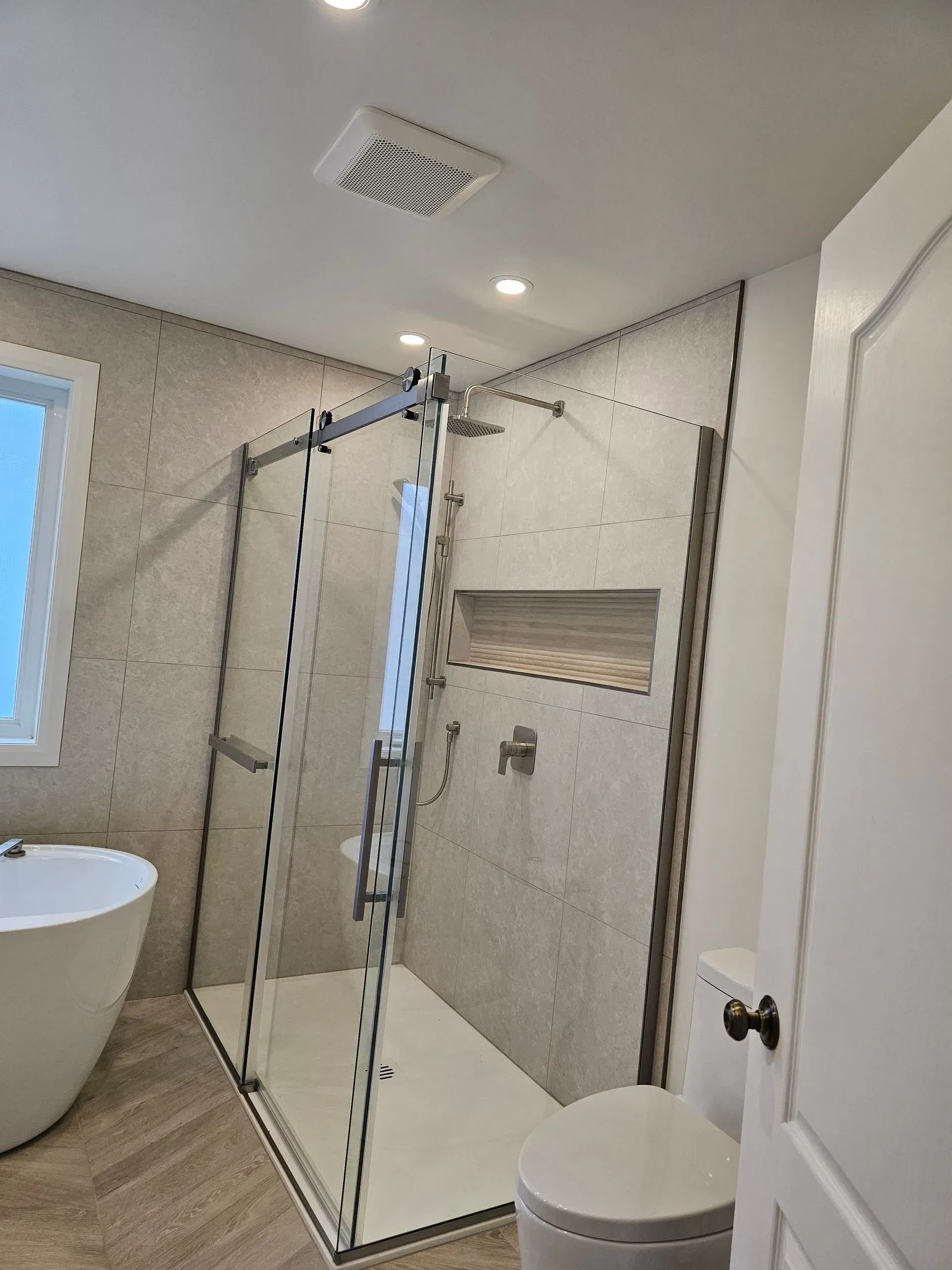 Salle de bains moderne avec douche en verre, carrelage blanc, baignoire îlot et toilettes