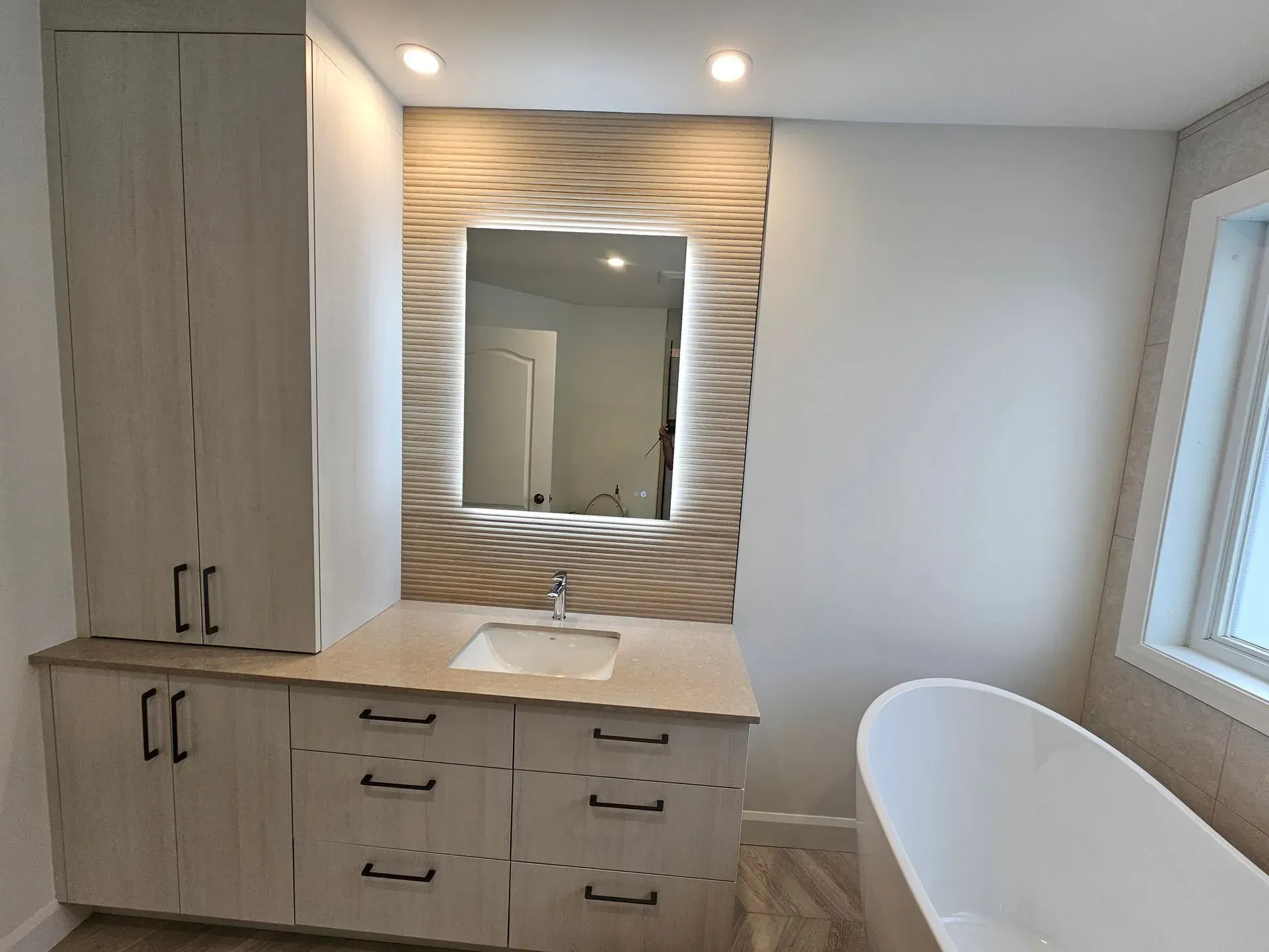 Meuble-lavabo moderne avec double vasque, grand miroir, armoires en bois et baignoire blanche près d'une fenêtre.
