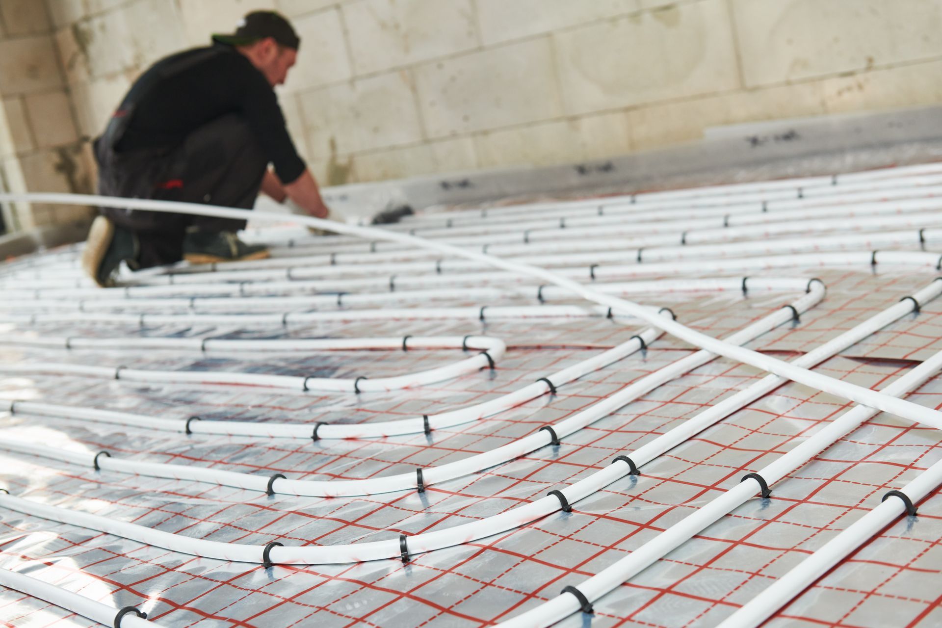 Ouvrier installant des tuyaux de chauffage au sol blancs sur un chantier de construction