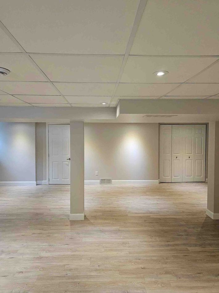 Pièce vide au sous-sol avec portes à panneaux blancs, une colonne de soutien et un sol en moquette beige
