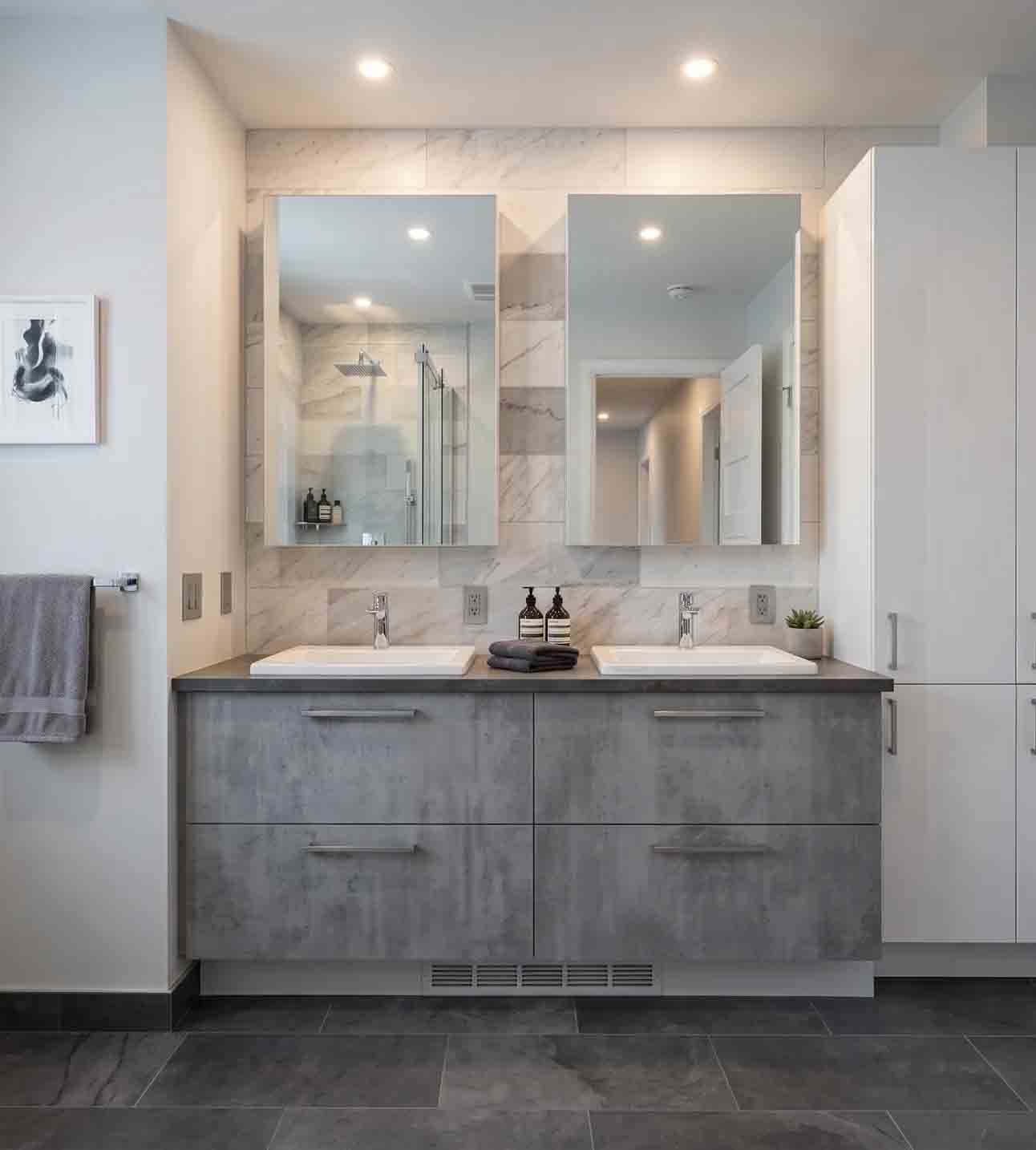 Meuble-lavabo moderne avec double miroir, armoires grises, comptoirs blancs et sol carrelé foncé.