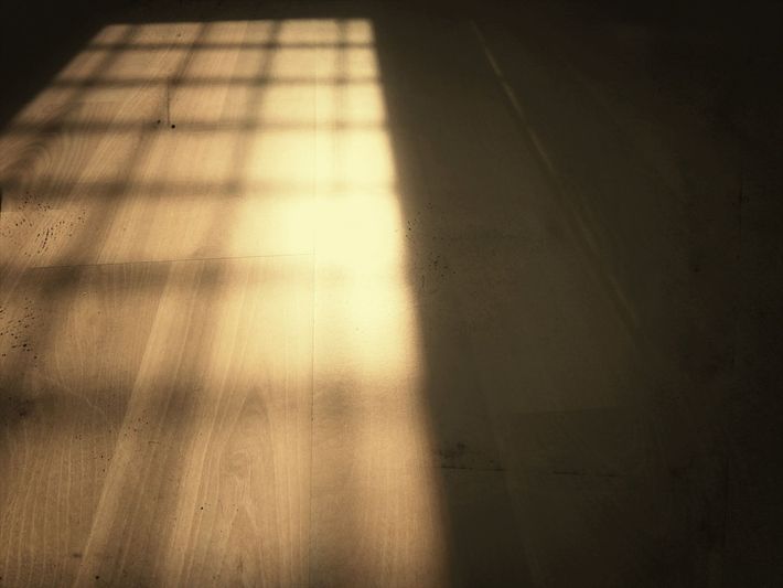 La lumière du soleil qui entre par une fenêtre projette une grille d'ombres lumineuses sur un plancher en bois.