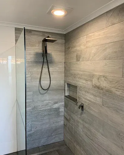 Modern walk-in shower with grey wood-look tiles, rainfall showerhead, and recessed shelf.— Rob Powell Plumbing Pty Ltd in Coraki, NSW