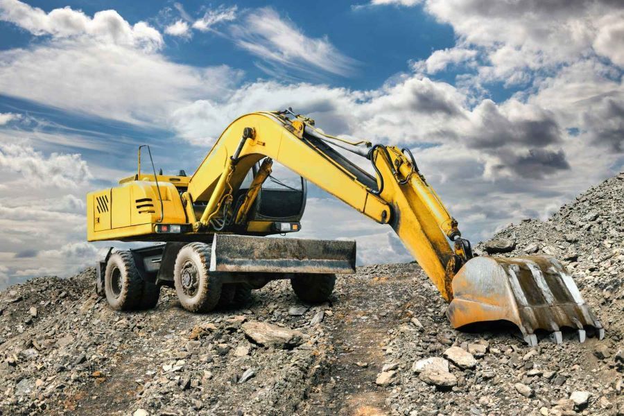Yellow Excavator on a Rocky Hill Under a Cloudy Blue Sky — Rob Powell Plumbing Pty Ltd in Coraki, NSW