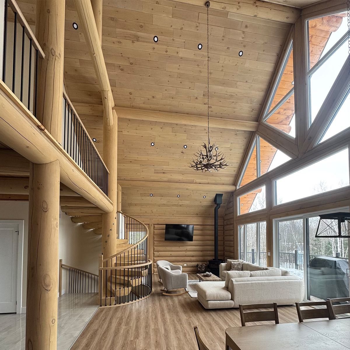 Rustic open-concept living room with wood walls, vaulted ceiling, chandelier, and large windows over sofas