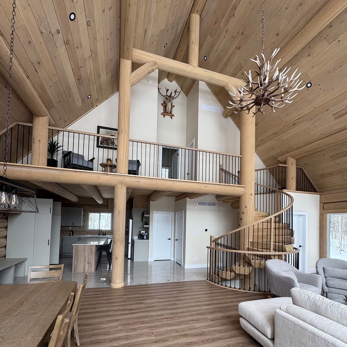 Rustic loft living room with vaulted wood ceiling, mezzanine, spiral staircase, and antler chandeliers