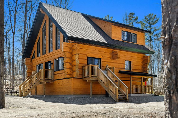 Cabane en rondins orange avec toit noir et escalier en bois dans une forêt enneigée sous un ciel bleu