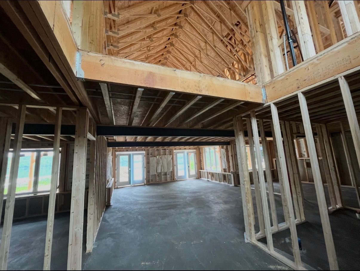 Interior of a house under construction with exposed wooden framing and unfinished concrete floor