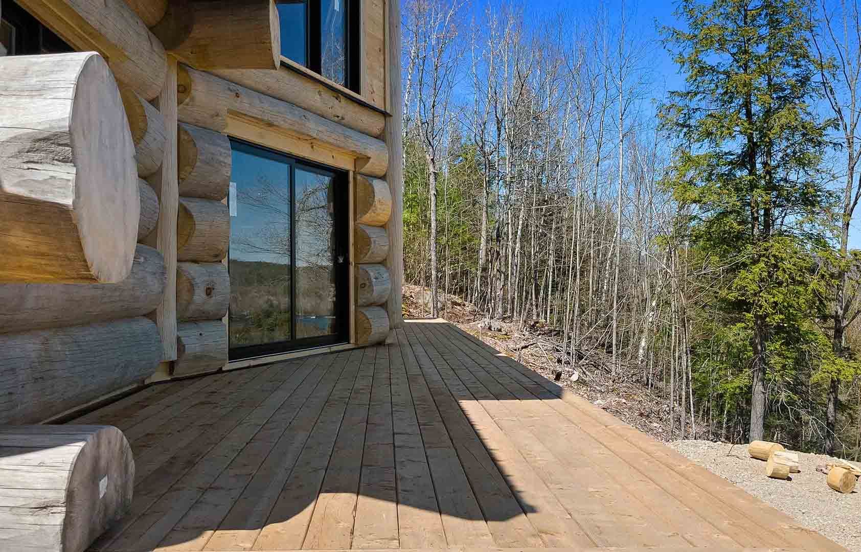 Wooden cabin deck beside sliding glass doors, with trees and a clear blue sky beyond.