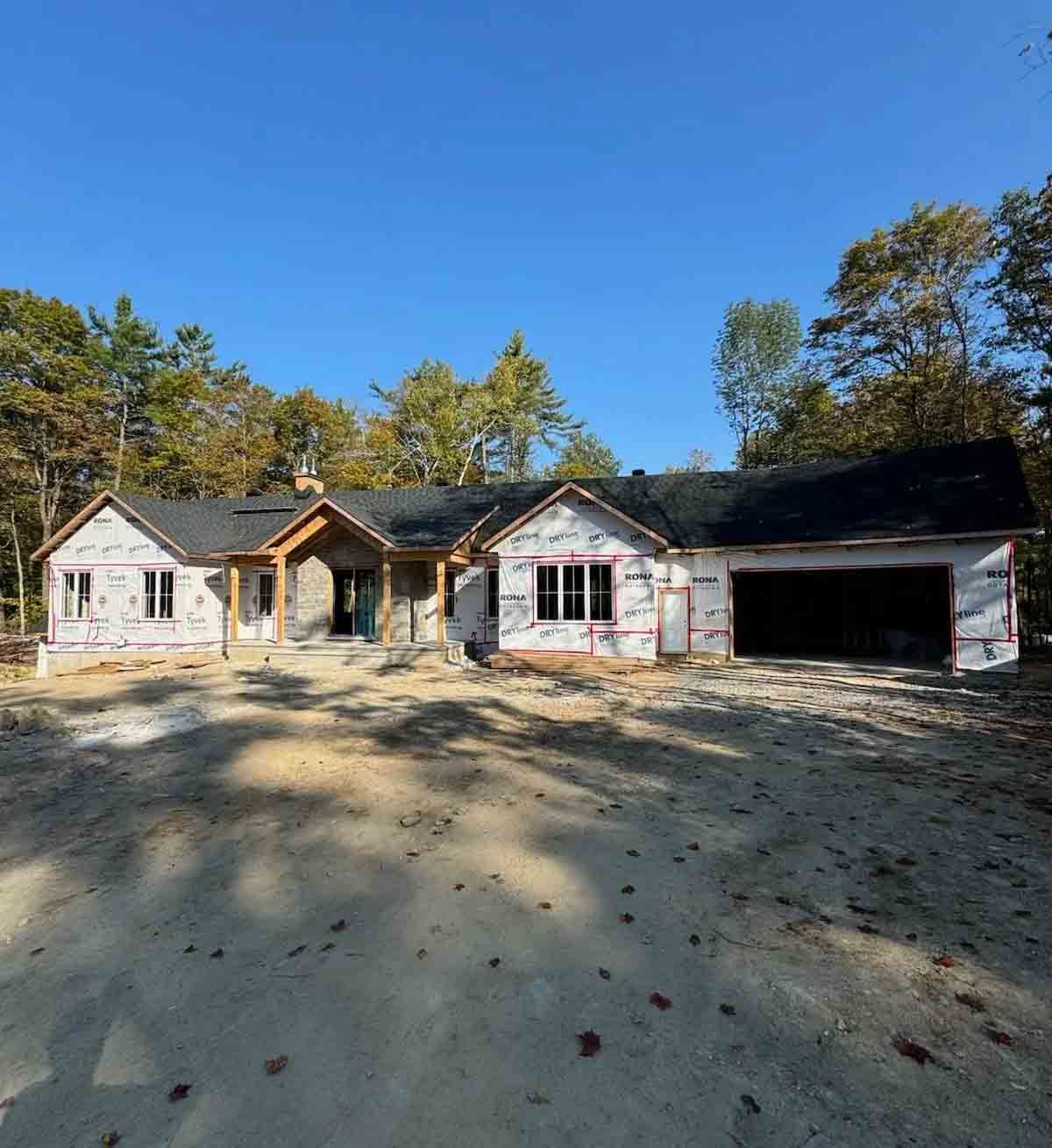Old white house with a front porch and open garage, set in a sandy yard with trees under a blue sky
