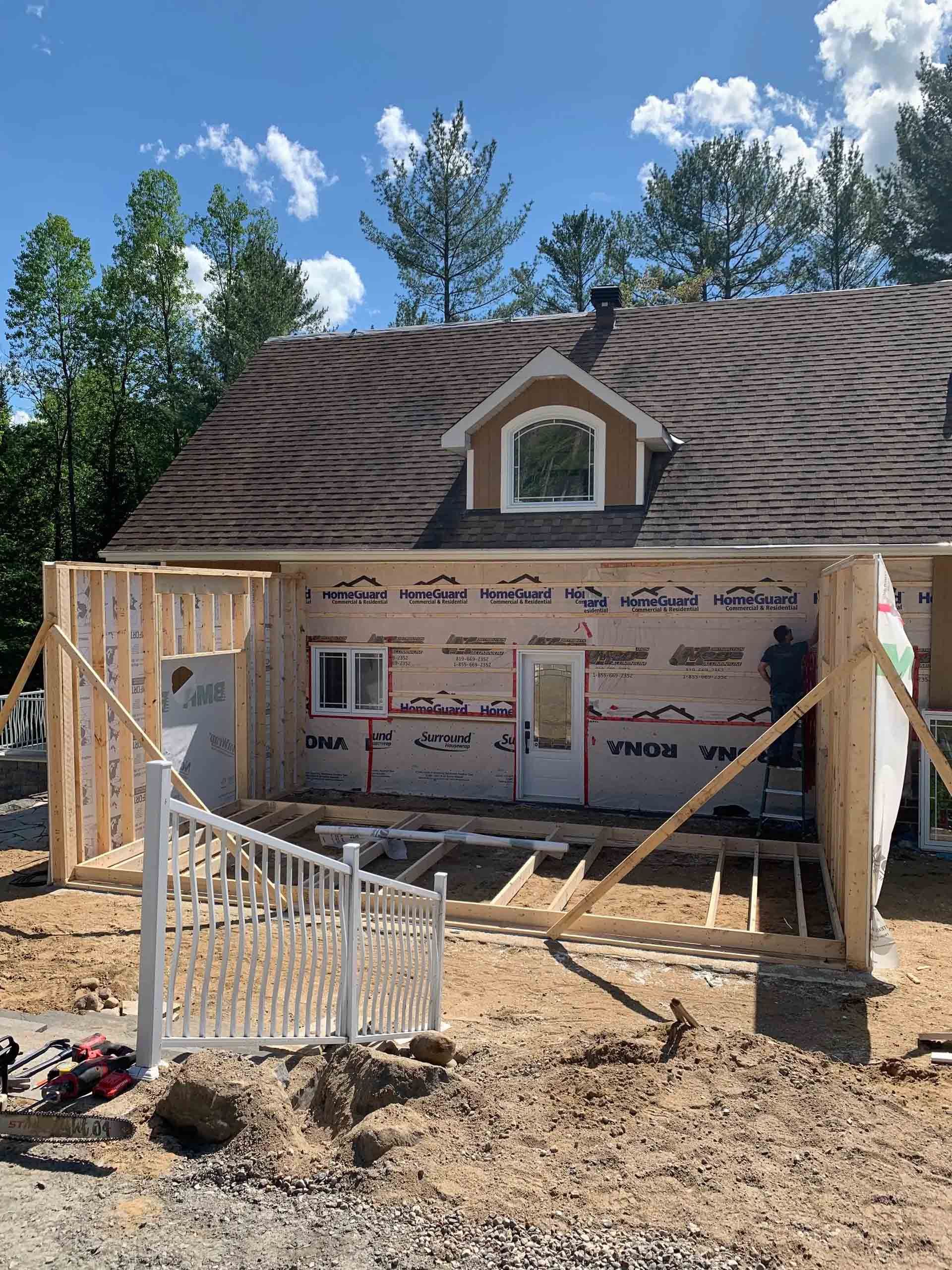 Partially built wooden porch frame in front of a house under a blue sky