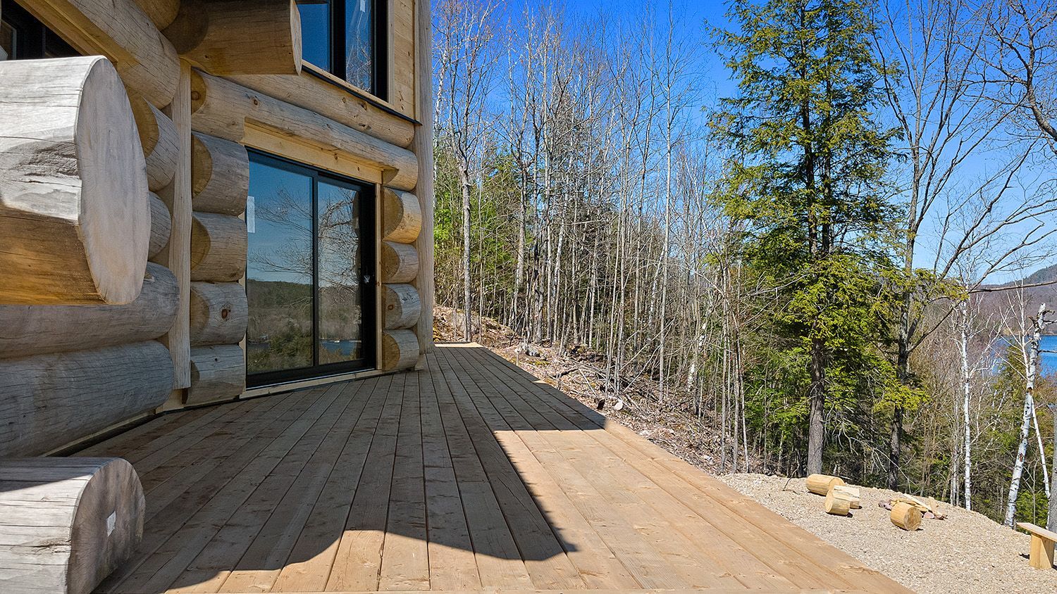 Wooden cabin deck with glass door, log exterior, and trees overlooking a valley